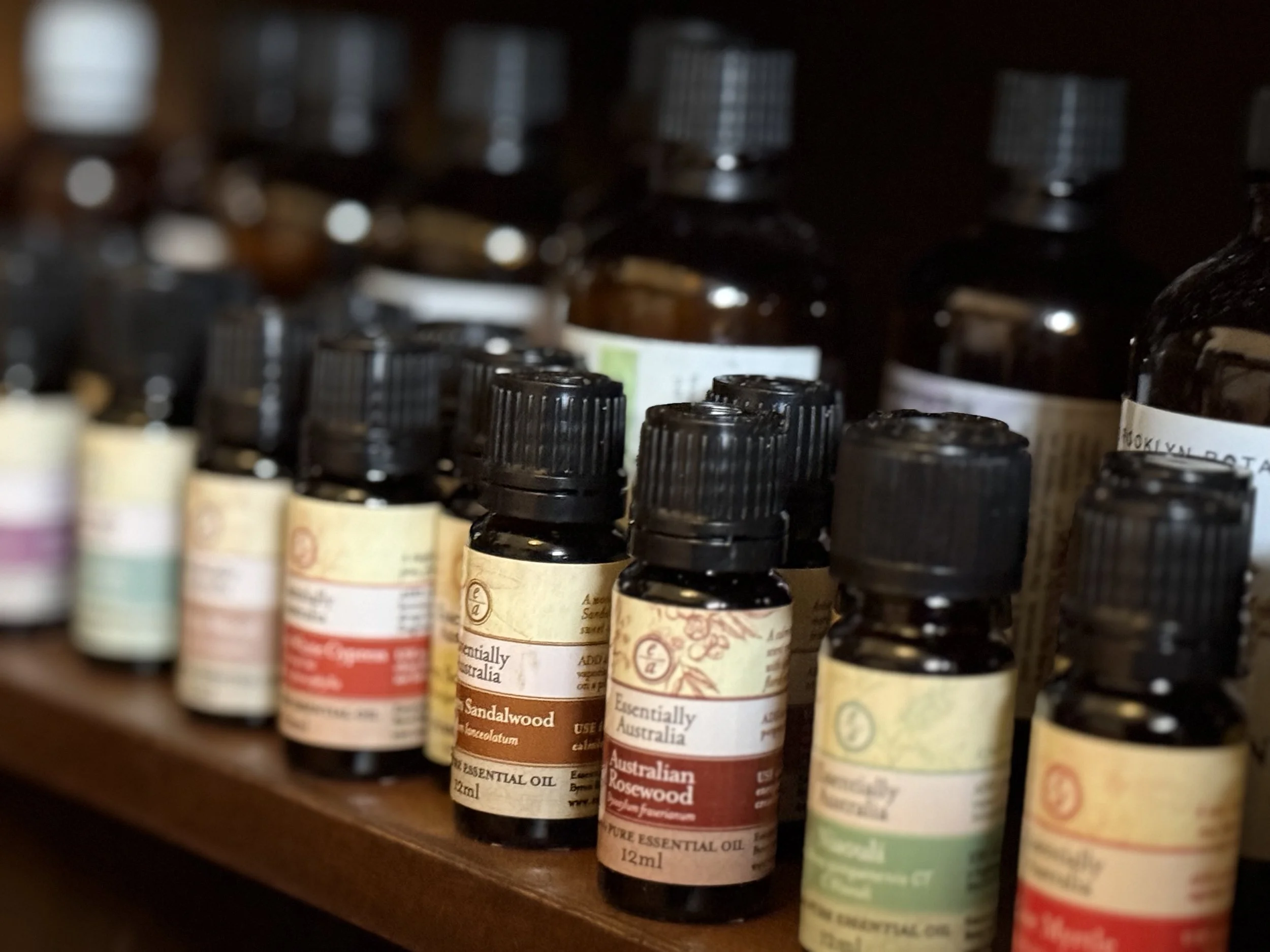 Shelf with several small bottles of essential oils, labels indicating scents like sandalwood and rosewood.