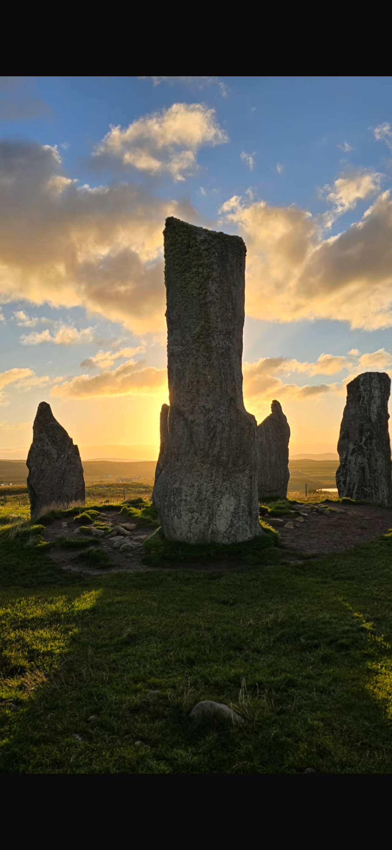 Sunset behind ancient standing stones on a grassy landscape.