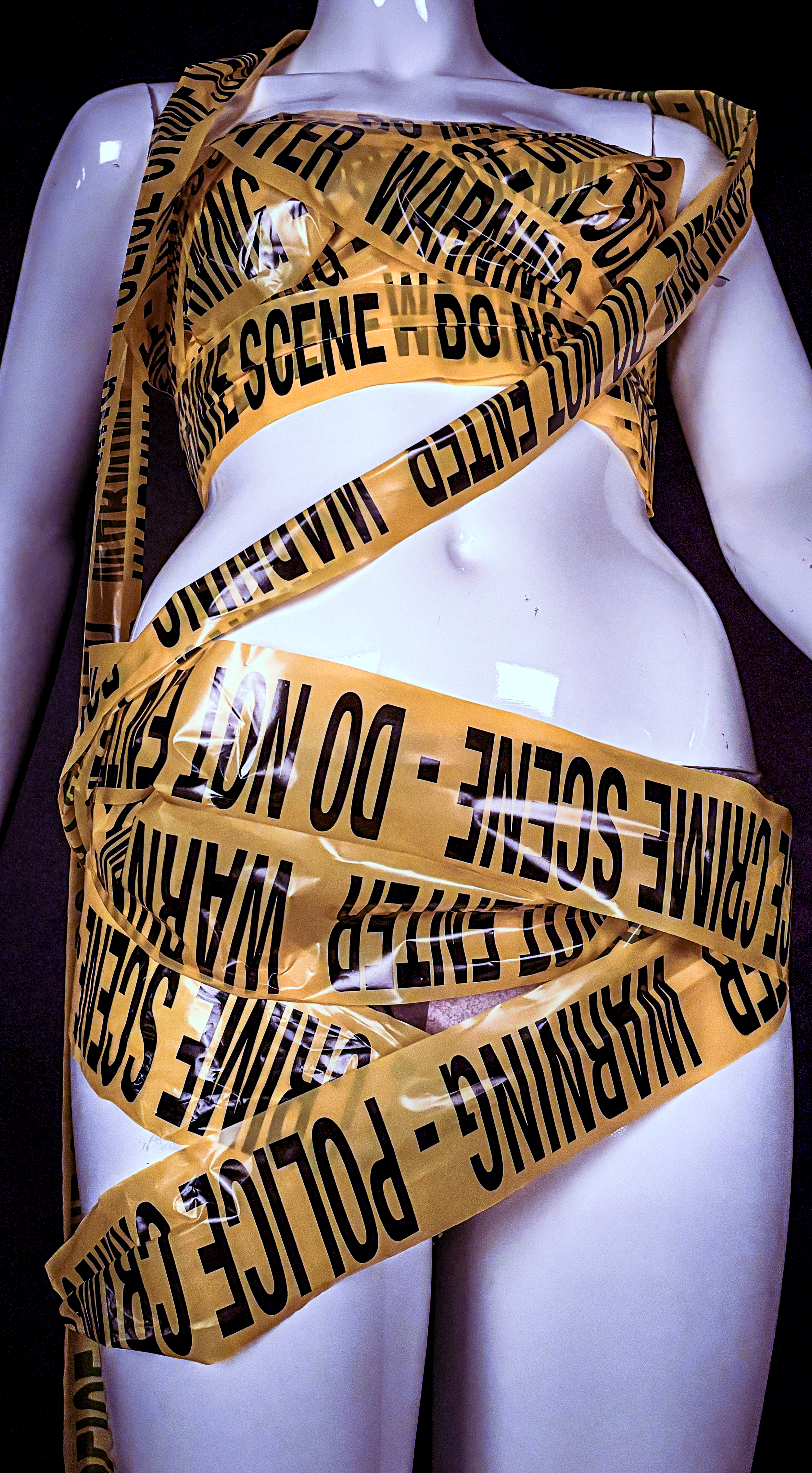 Partially clothed mannequin wrapped in yellow caution tape with black text reading 'crime scene do not cross'.