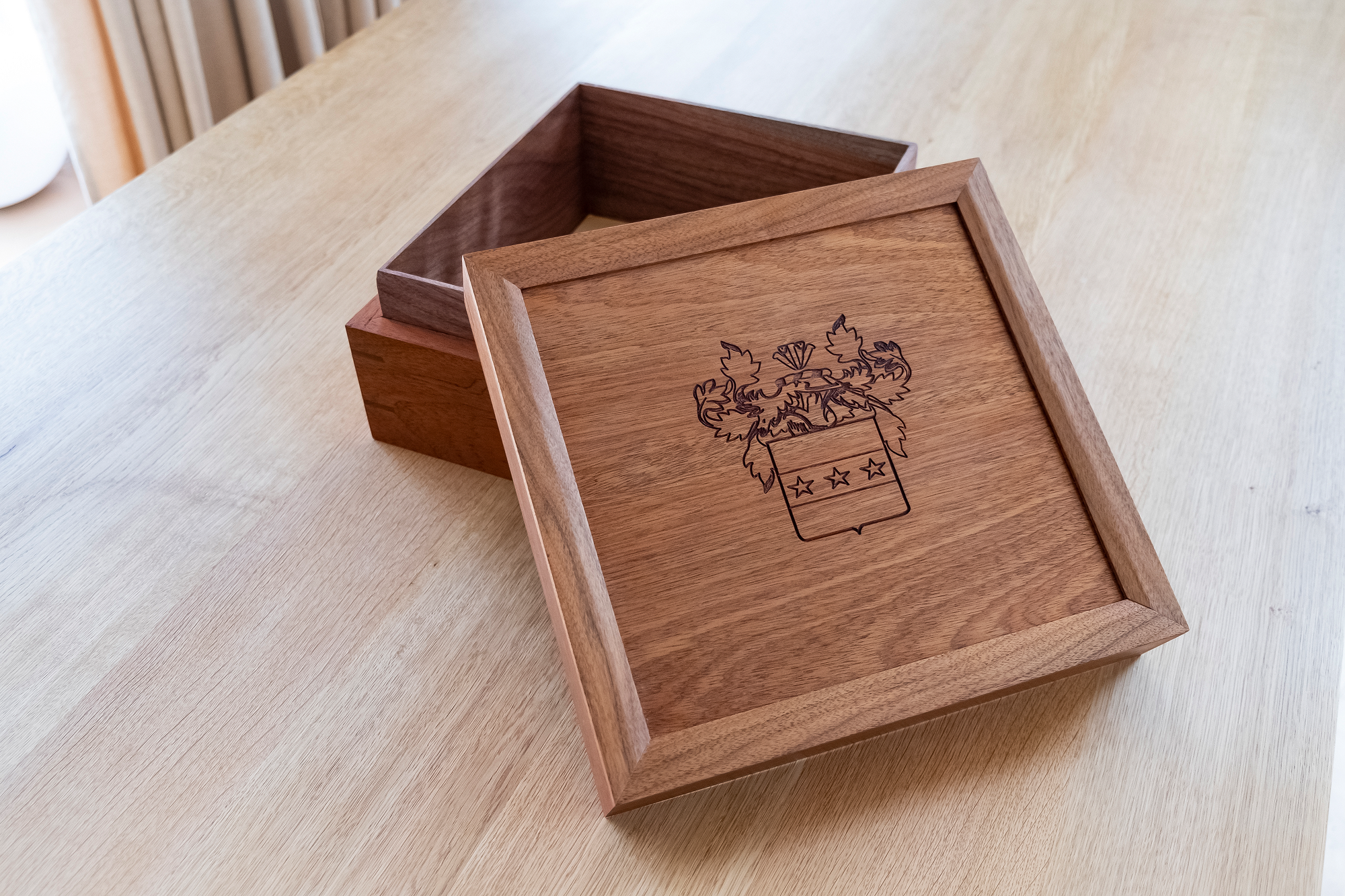 A wooden box with a lid featuring an engraved design of a family crest at Adam Stone Furniture.