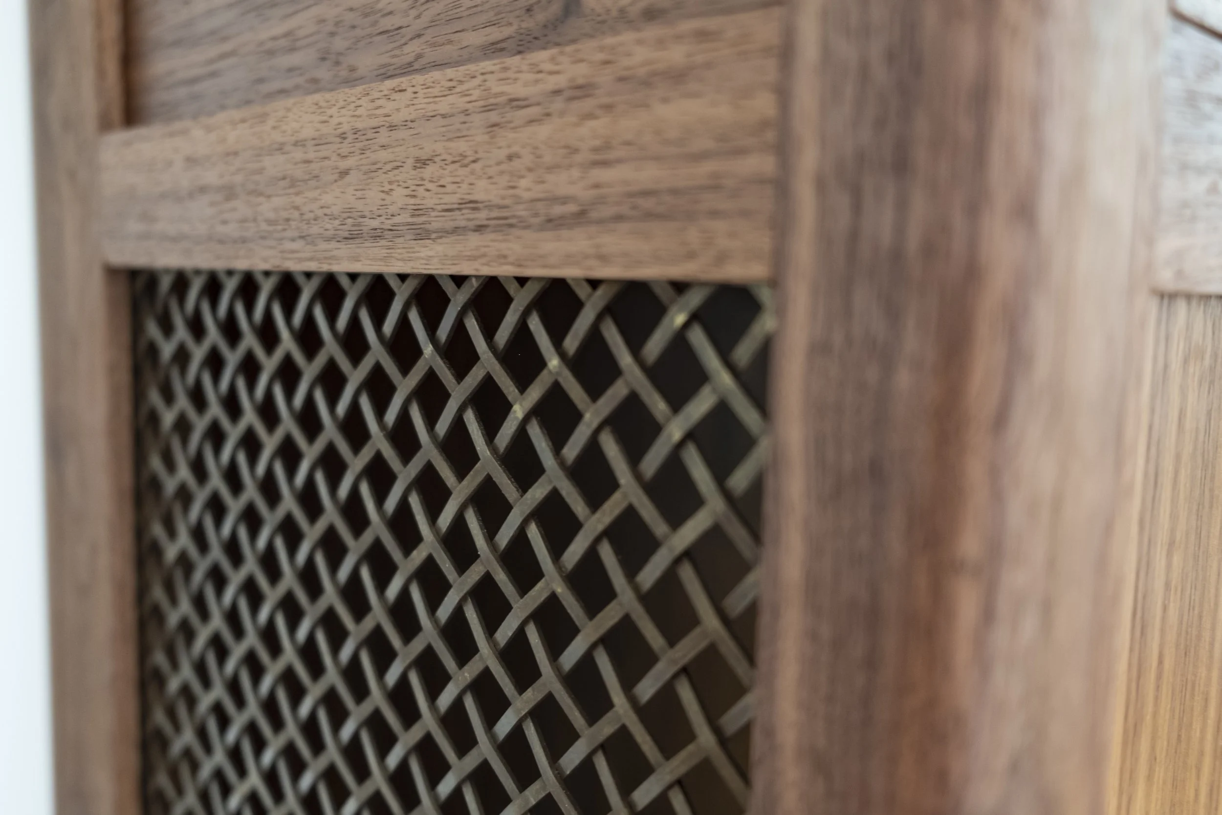 Close-up of a wooden, walnut cabinet with a brass metal mesh side panel at Adam Stone Furniture.