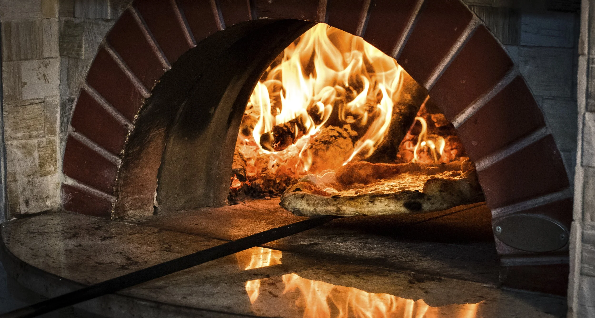 eine fertige pizza wird aus einem mit holz befeuerten pizzaofen geholt