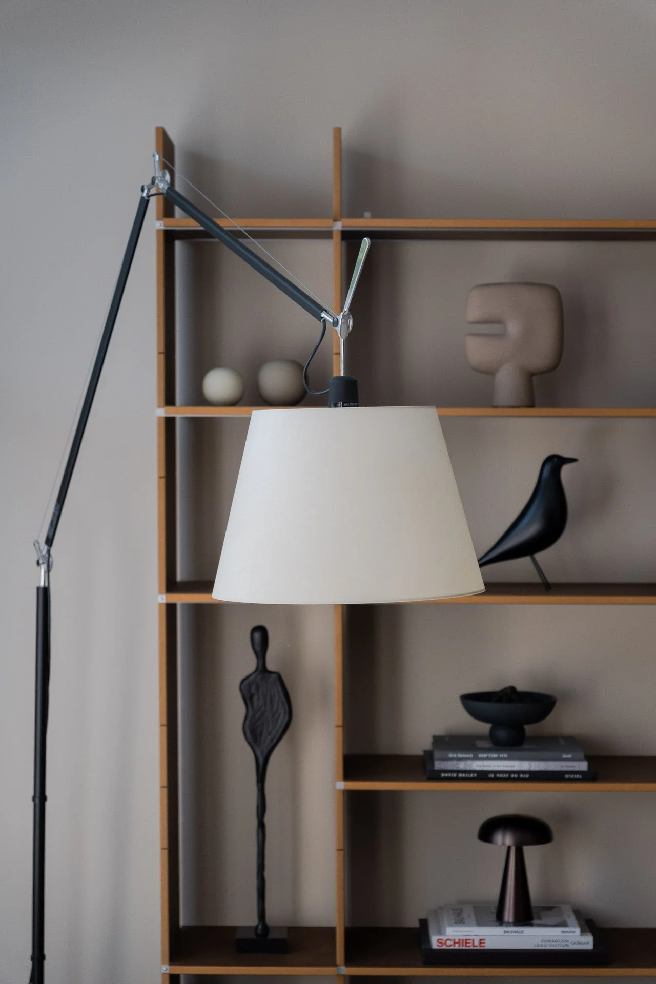 Interior scene with a wooden bookshelf, decorative objects, sculpture, and a black chair, partially obscured by a white lampshade and a black floor lamp.