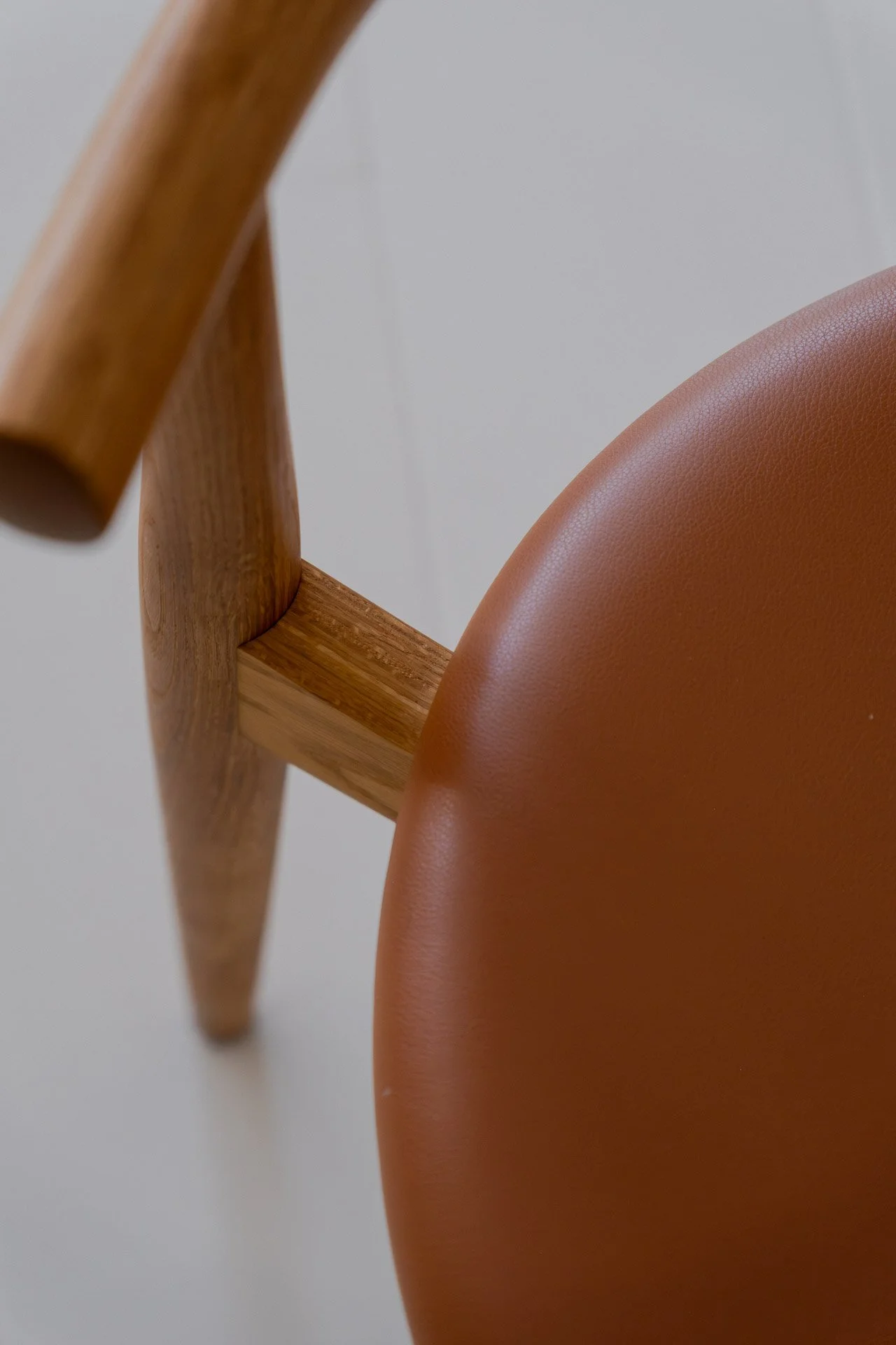 Close-up of a wooden chair with an orange leather seat against a plain light background.