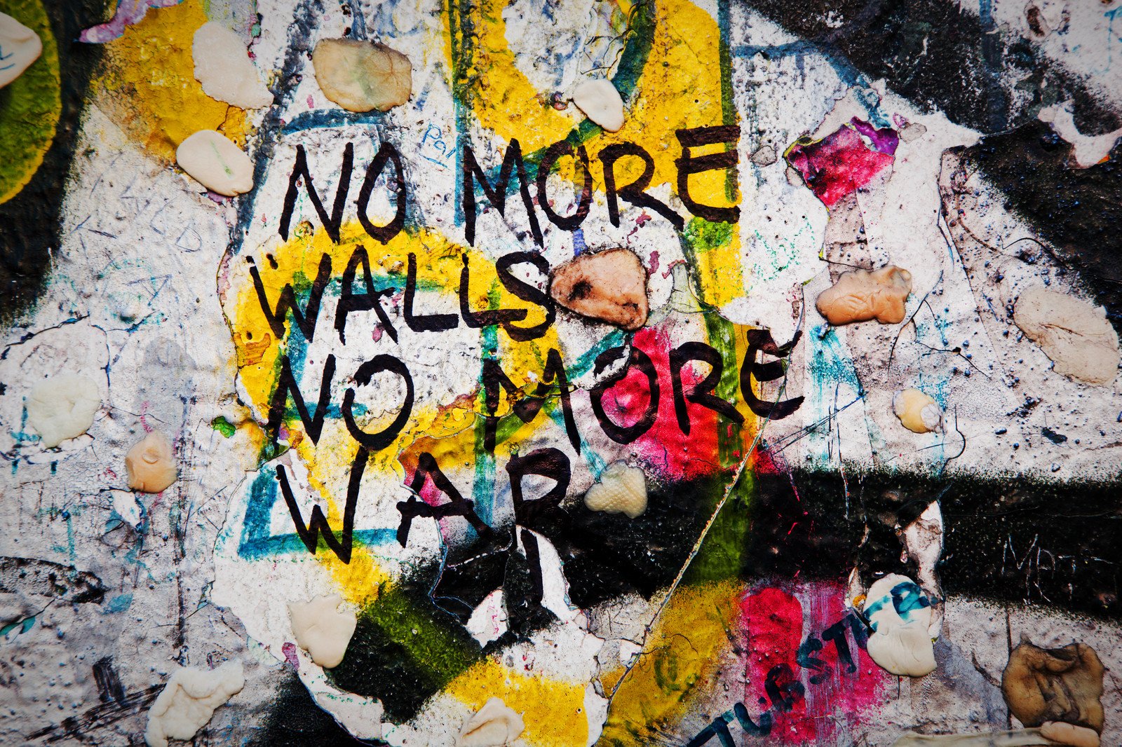 Straßenkunst mit der Botschaft 'NO MORE WALLS, NO MORE WAR' auf einer bunten, zerkratzen Wand mit Lichthöhlern und Aufklebern.