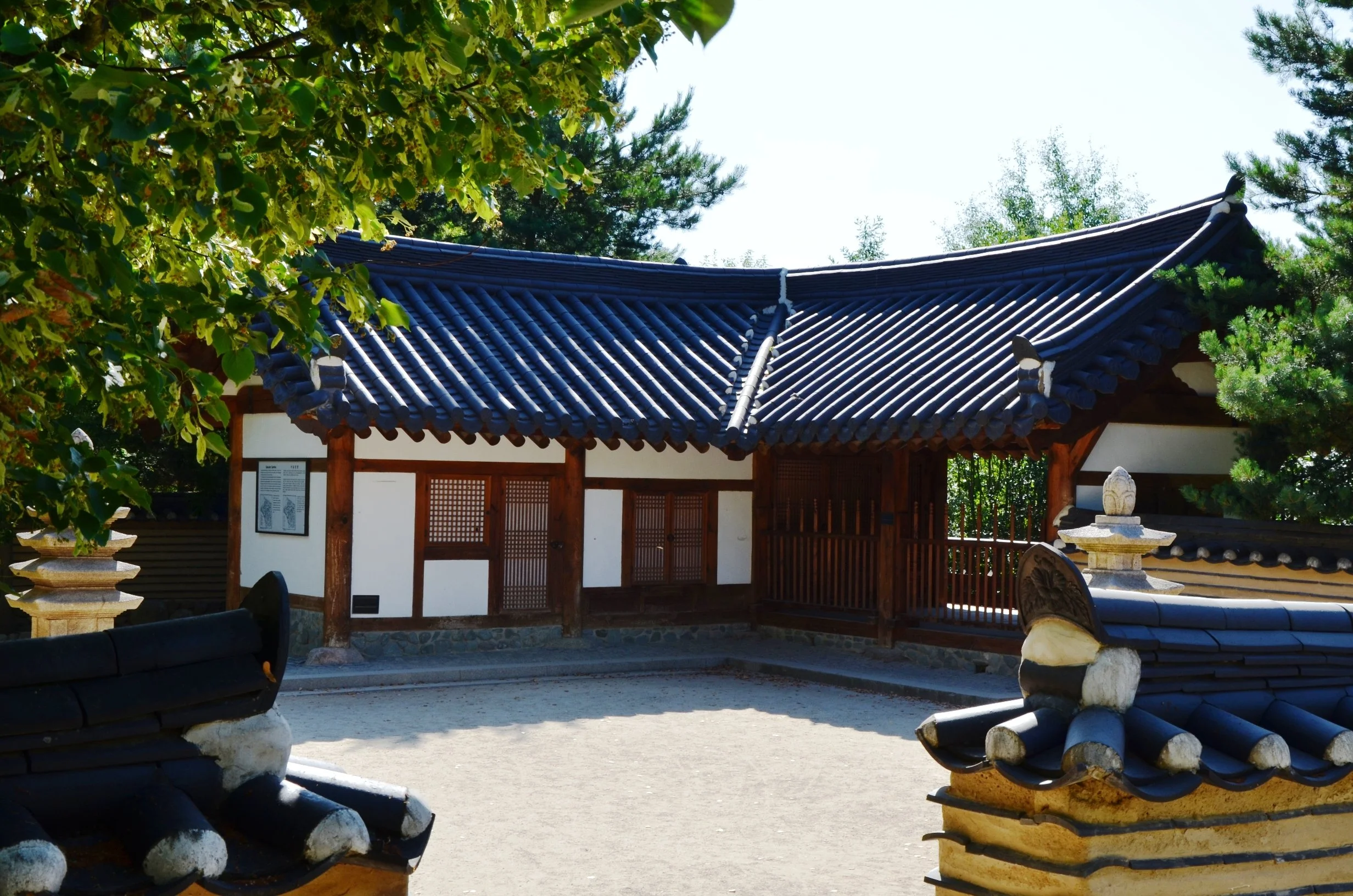 Traditionelles koreanisches Gebäude mit blauer Ziegeldach, umgeben von grünen Bäumen und einem Steinbrunnen im Vordergrund.
