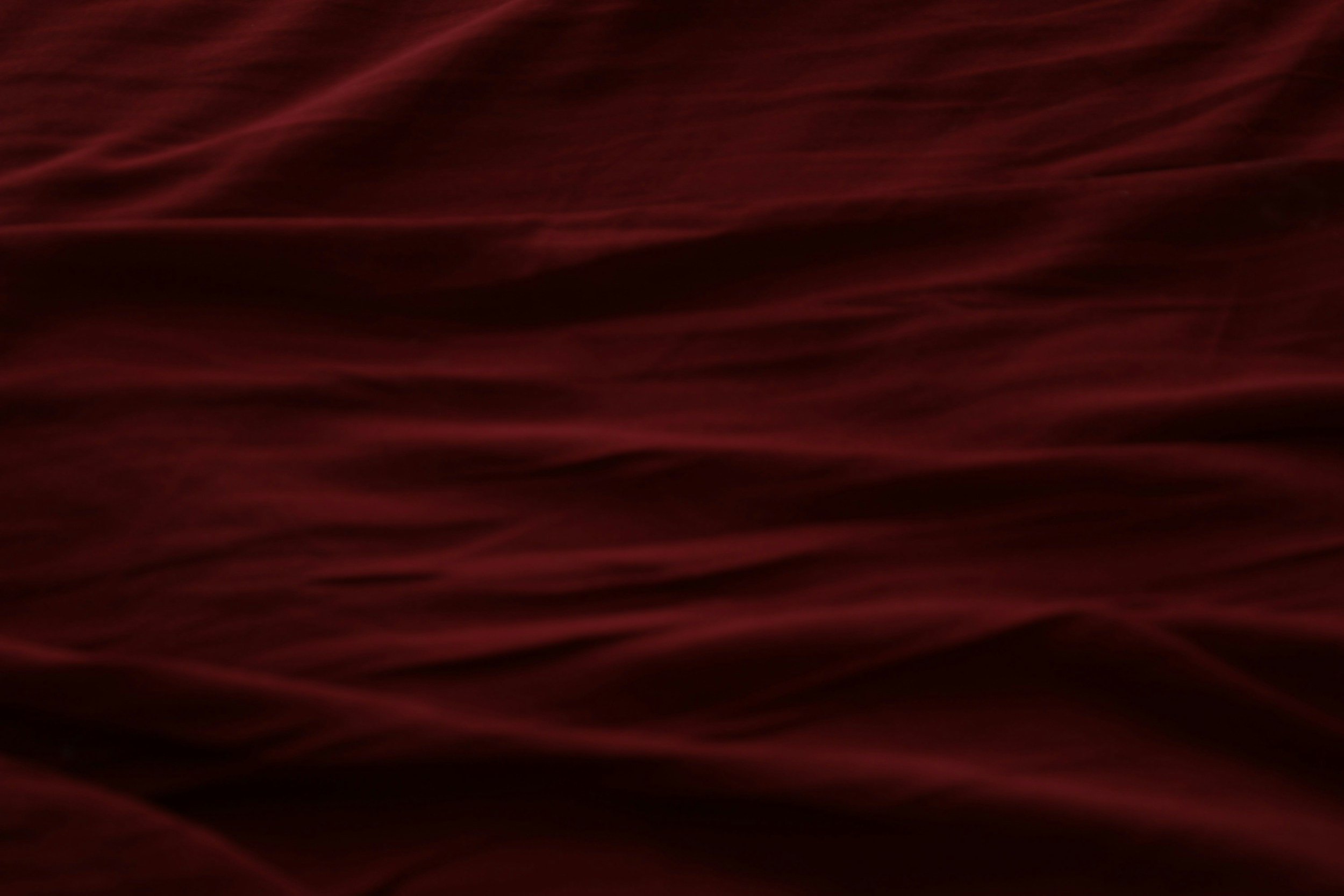 Deep red and black abstract background with flowing, wave-like patterns.