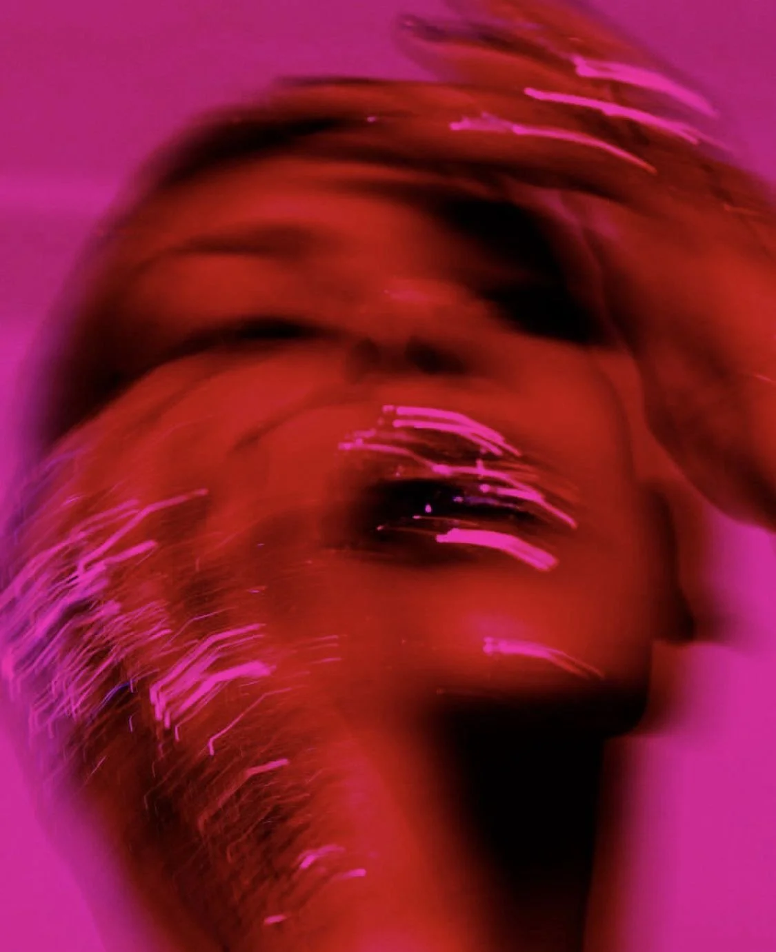 Close-up of a person's face with artistic pink and red lighting effects, creating a blurred and abstract appearance.