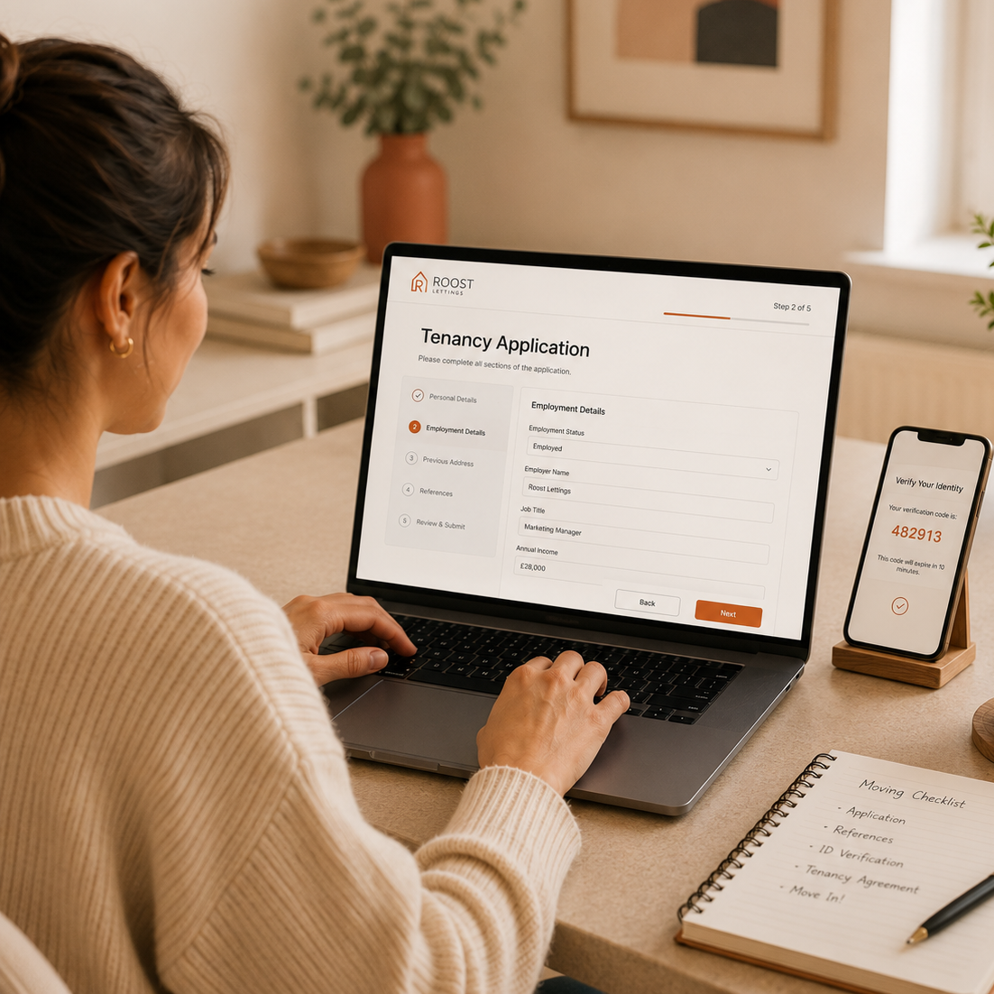 A woman completes a tenancy application on a laptop with a smartphone and a notebook nearby, in a cozy home office.