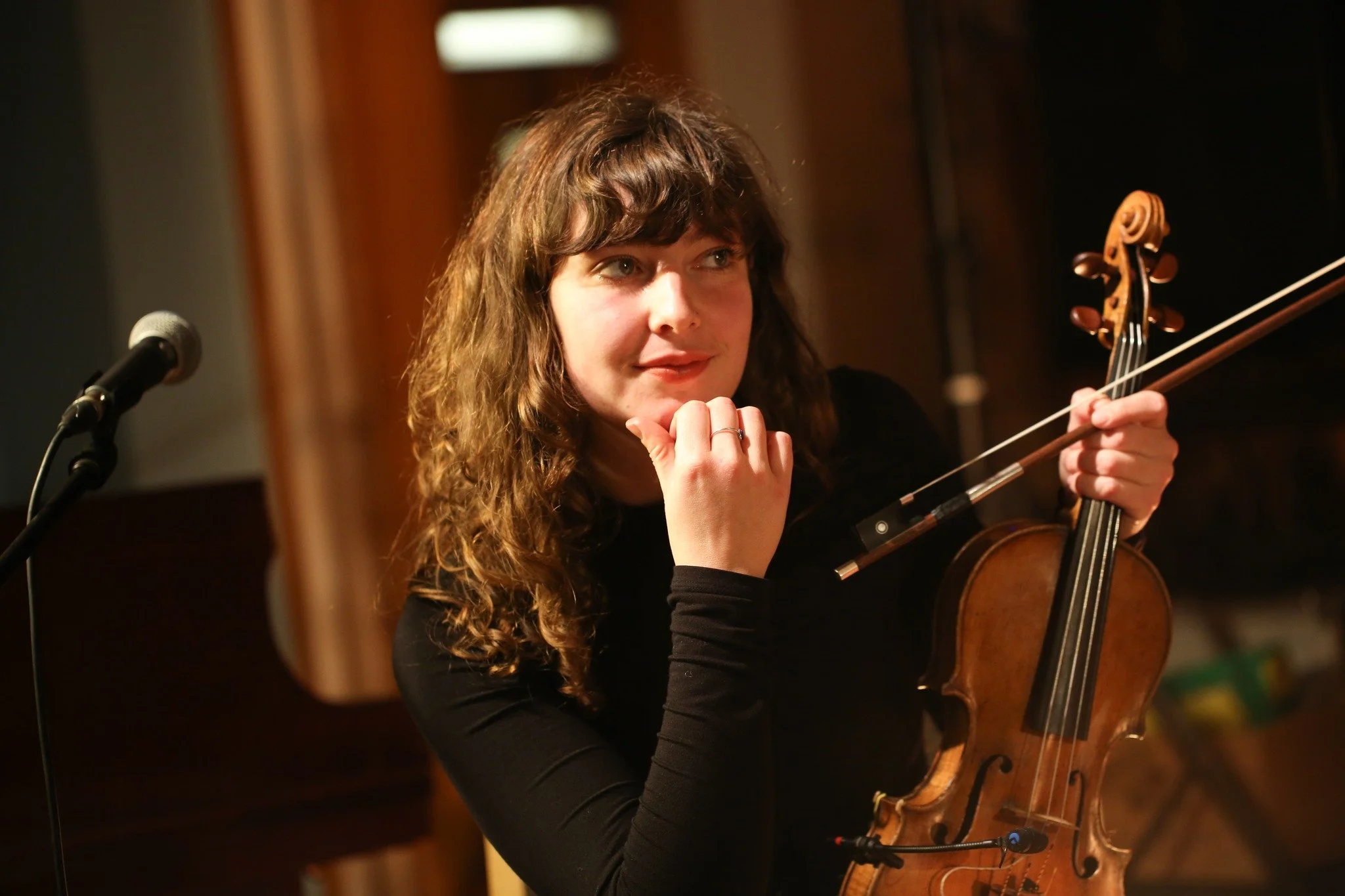 A woman with curly brown hair and a thoughtful expression holding a violin