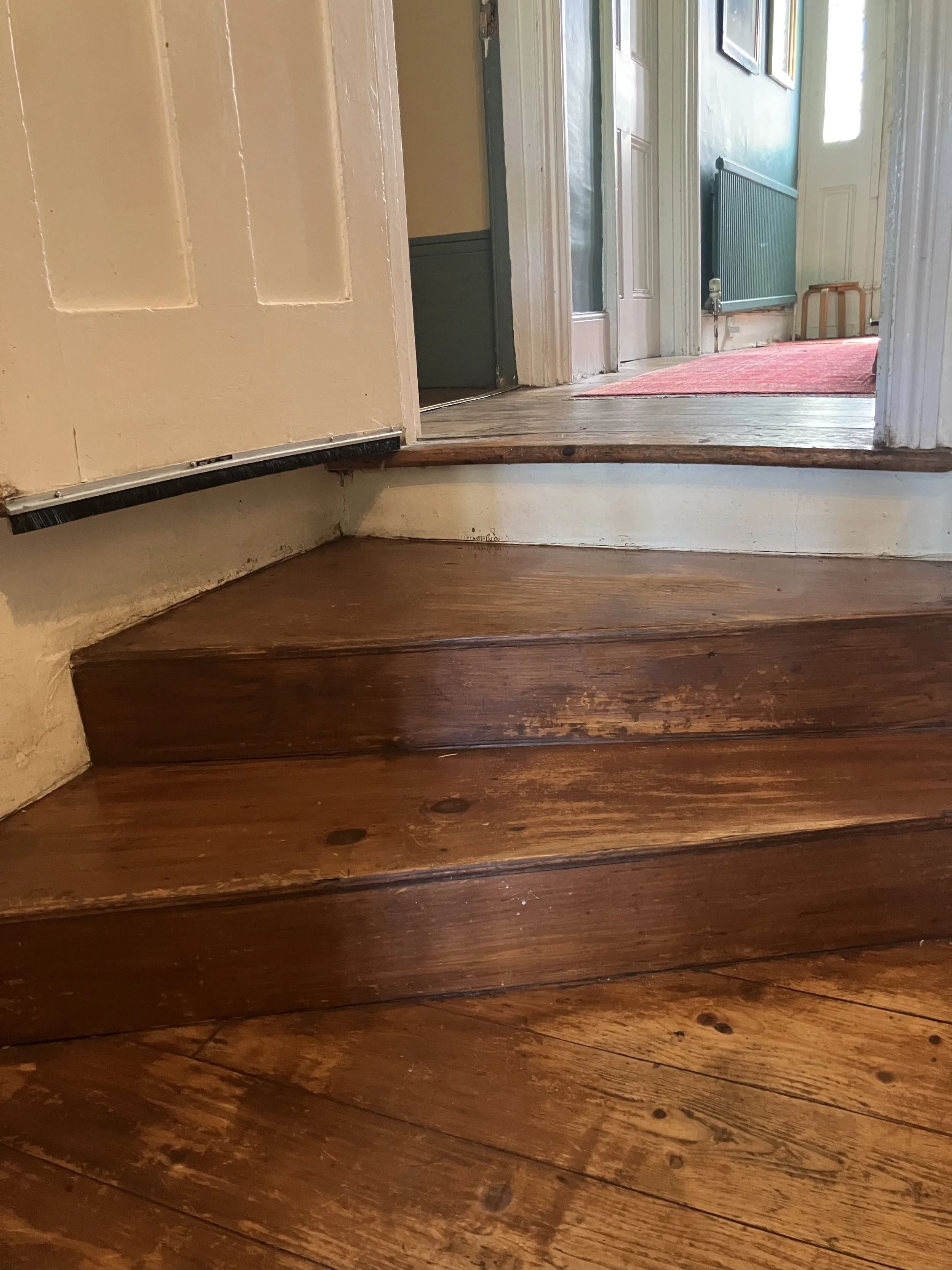 Close-up view of 2 wooden stairs, leading up to a doorway in a house interior.