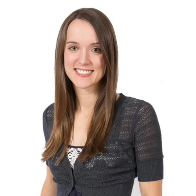 Professional headshot of a smiling woman with long straight brown hair, wearing a dark knitted cardigan against a white background.