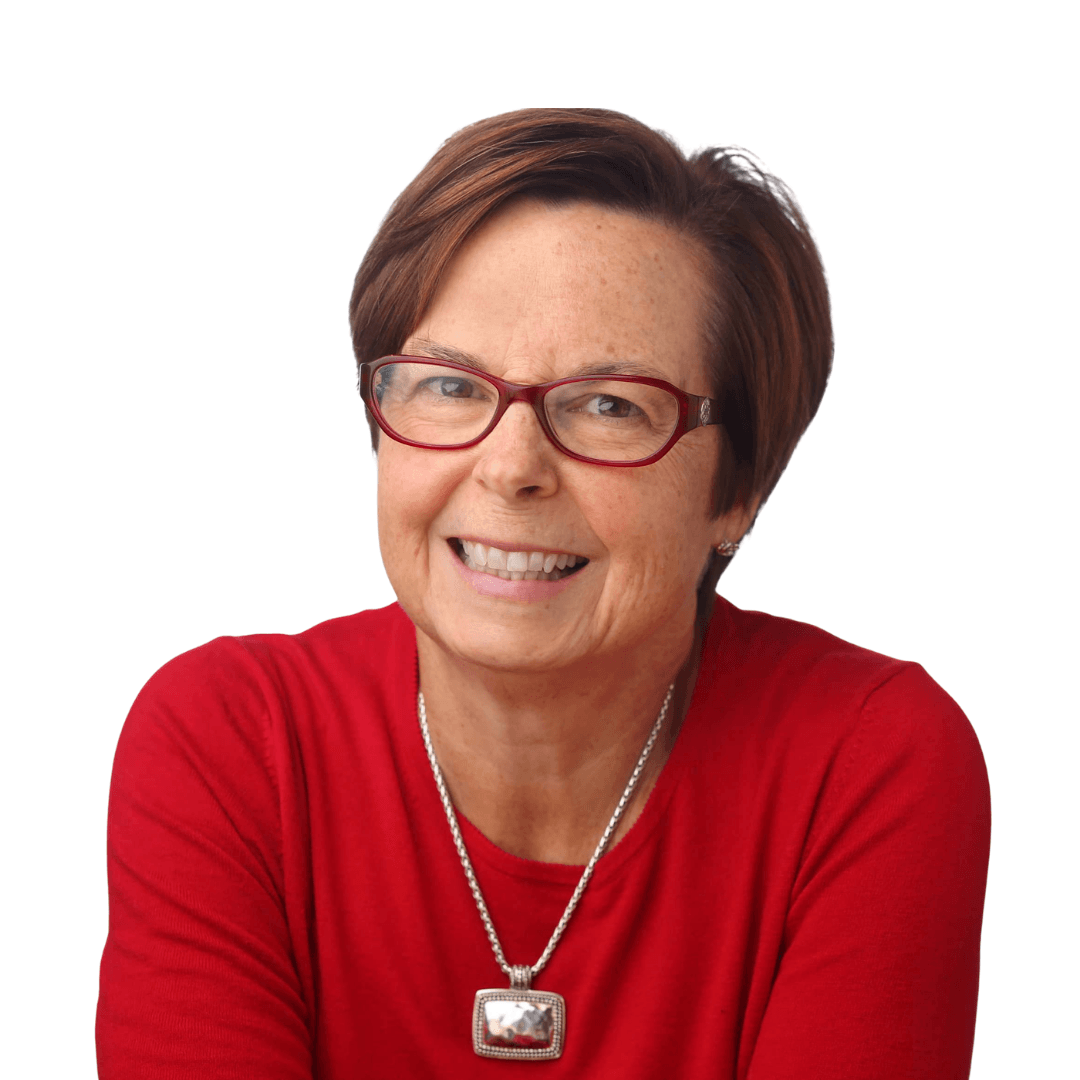 Professional headshot of a smiling woman with short auburn hair and red glasses, wearing a red top and silver pendant necklace against a white background