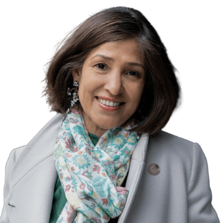 A person with dark shoulder-length hair smiles while wearing a floral scarf and a light-colored jacket