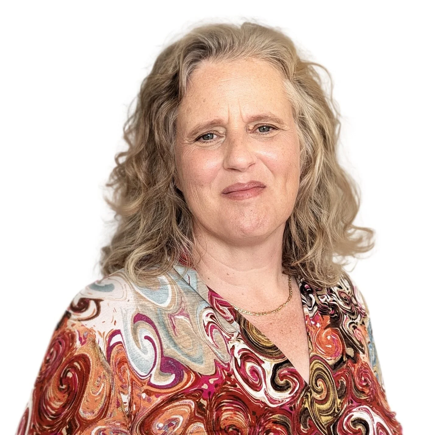 Professional headshot of a woman with shoulder-length wavy blonde hair, wearing a colourful patterned blouse against a white background.