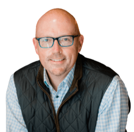 Professional headshot of a smiling bald man with glasses and a short beard, wearing a checked shirt and dark quilted vest against a white background