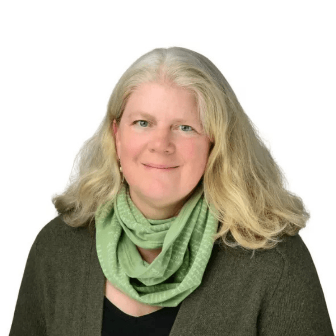 Professional headshot of a smiling woman with long blonde-grey hair, wearing a green scarf and dark cardigan against a white background