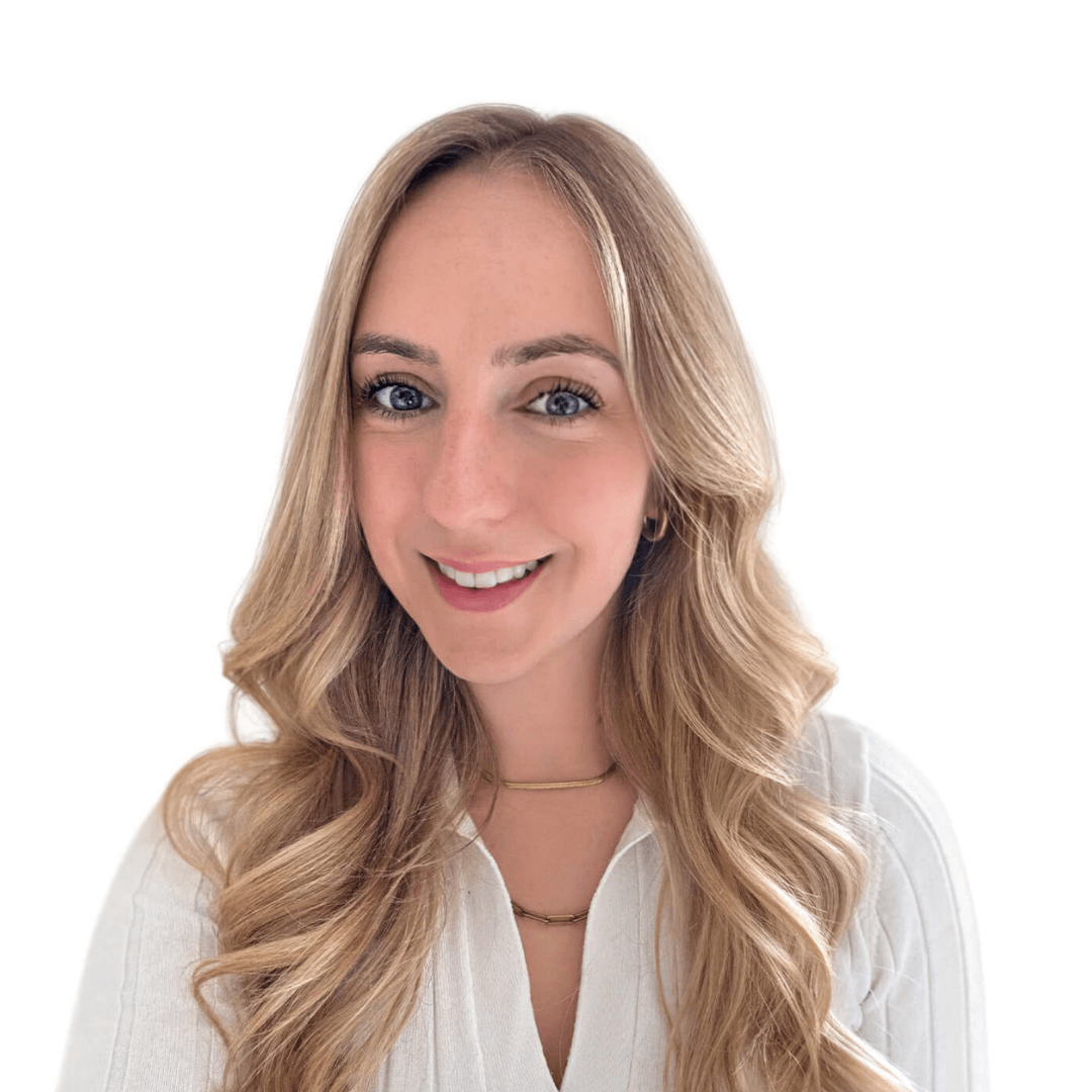 Professional headshot of a smiling woman with long, wavy blonde hair, wearing a white blouse and delicate gold necklaces, against a plain white background.