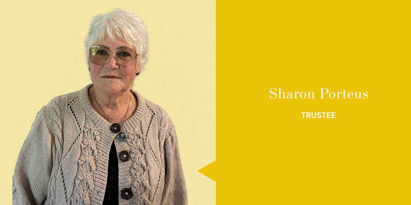 Portrait of Sharon Porteus, an older woman with short white hair, wearing glasses, a beige cable-knit cardigan with large buttons, and a necklace, standing against a yellow background with her name and title as trustee displayed.
