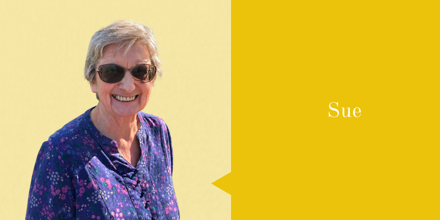 A smiling elderly woman wearing sunglasses and a purple floral blouse, standing against a light yellow background, with a yellow message box next to her that says Sue.