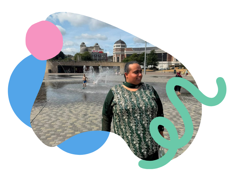 Woman standing near a fountain in an urban plaza with a domed building and a bridge in the background.