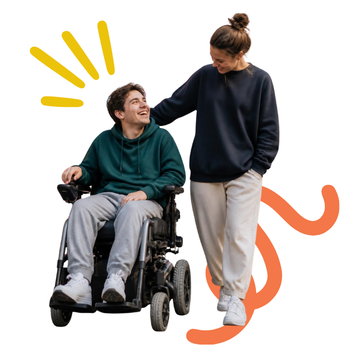 A young man in a wheelchair smiling and looking up at a young woman standing beside him, who is smiling and looking down at him, both dressed in casual clothing.