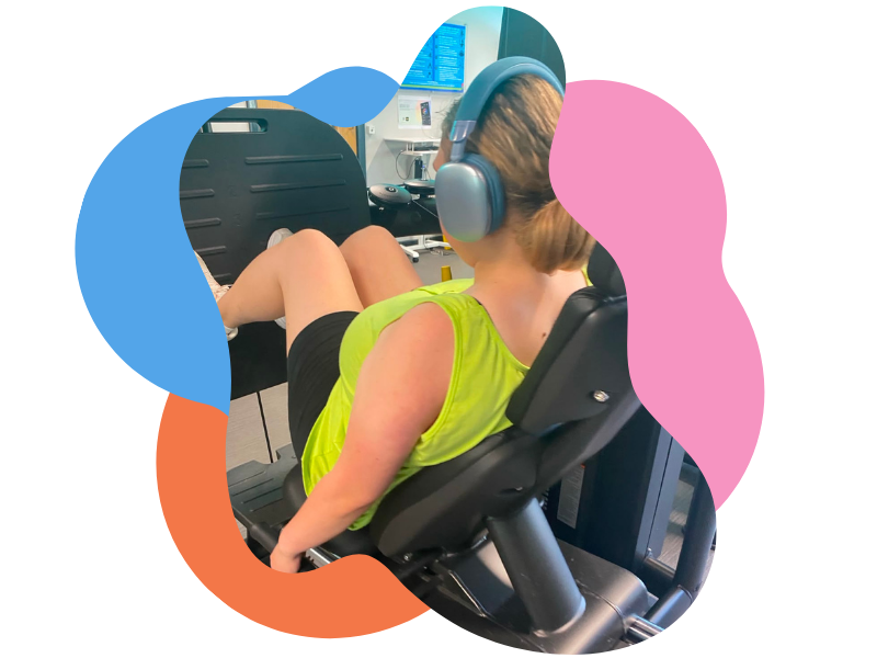 Person listening to headphones while reclining in a medical or research chair in front of computer monitors.