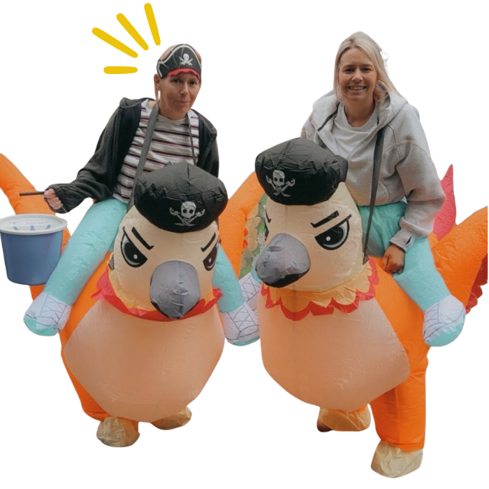 Two women in colorful inflatable pirate-themed costumes with parrots, smiling and posing for the photo.