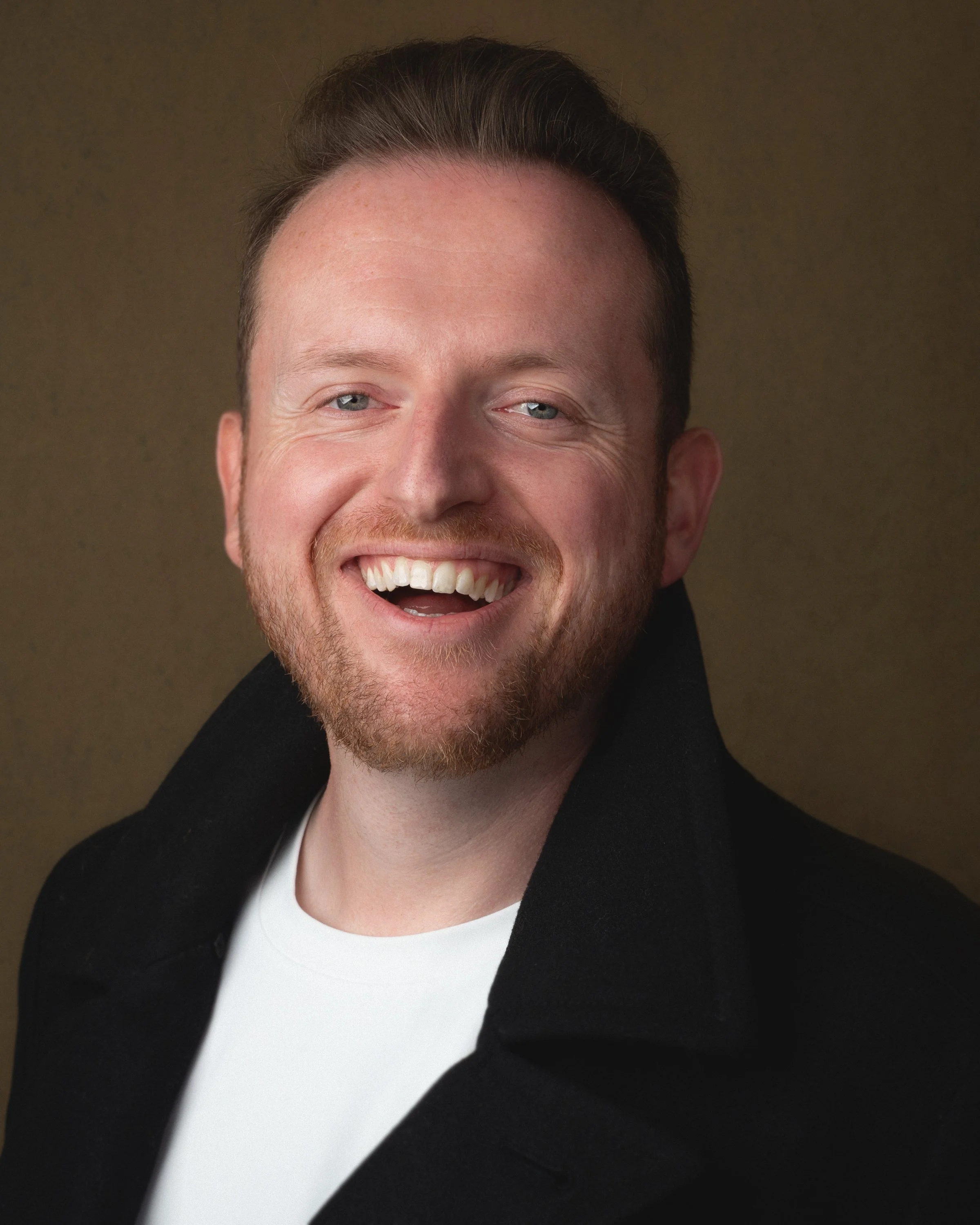 Headshot of Greg Link wearing a white t-shirt with a black jacket