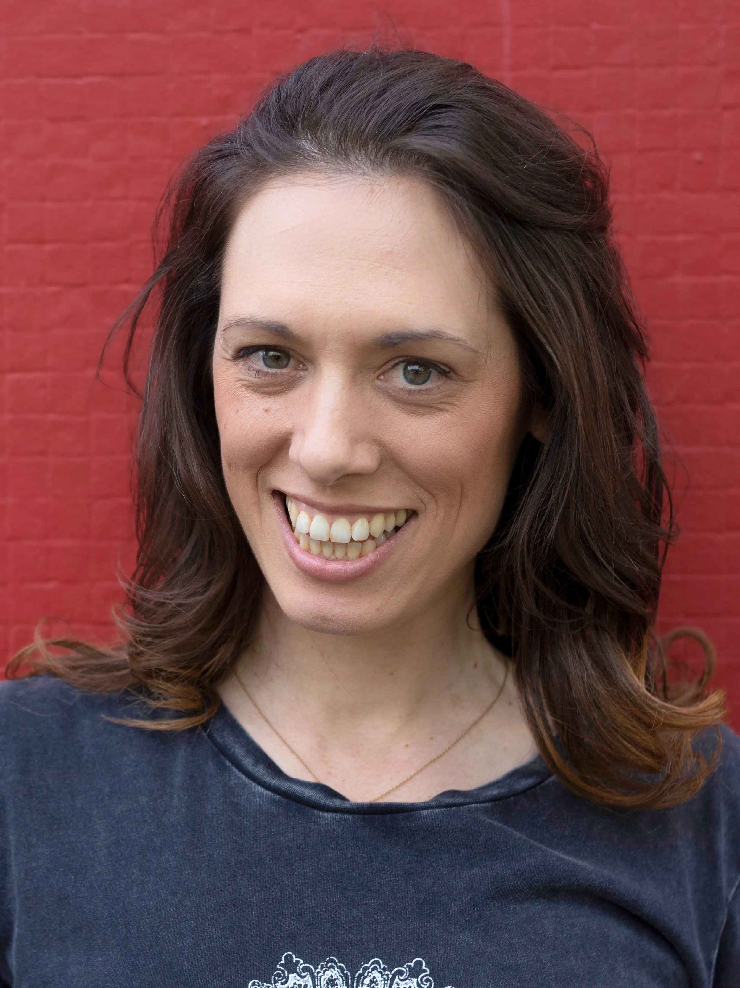 Headshot of Caitlyn Burt wearing a grey t-shirt with a red brick background