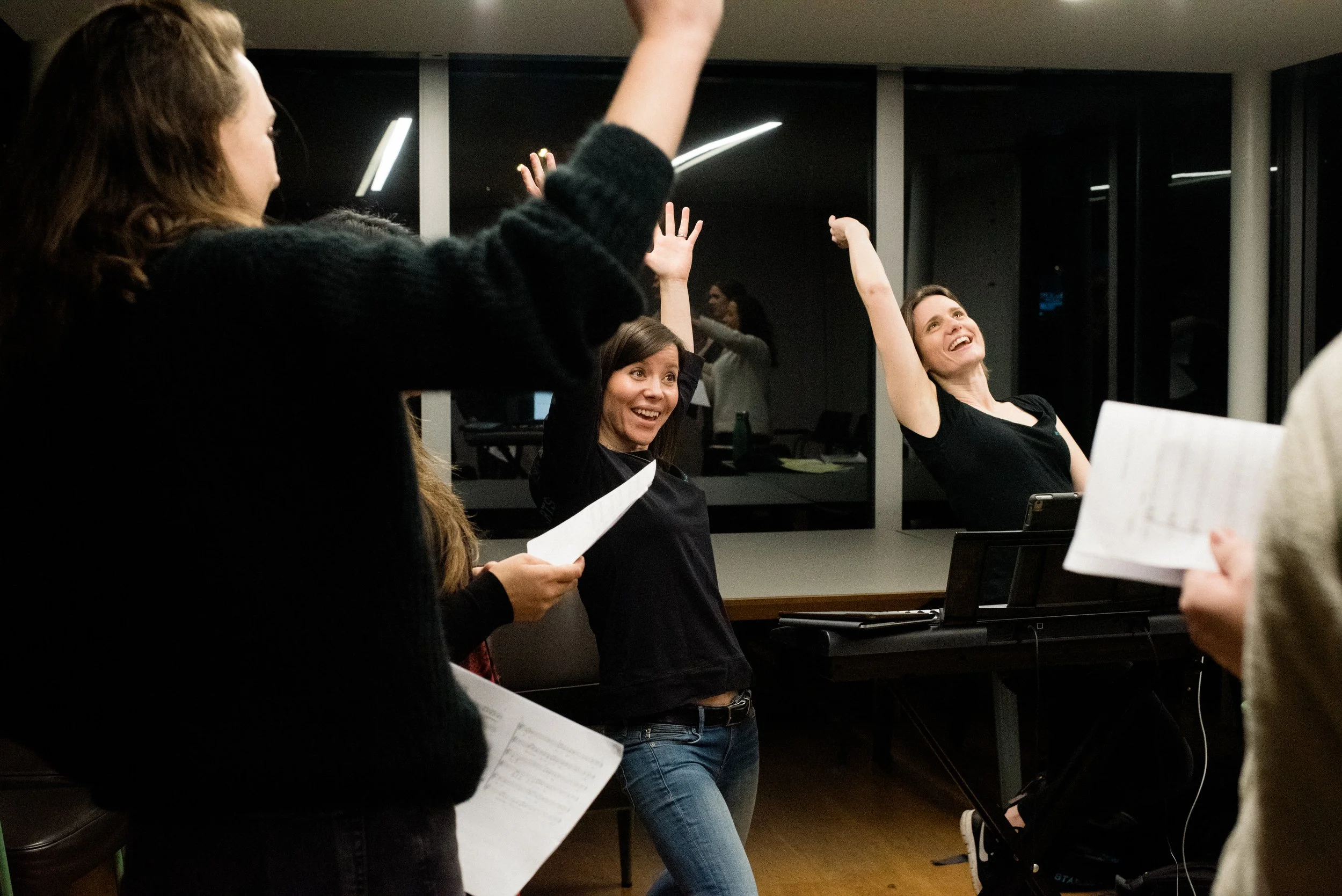 Emily & Anna, directors of Starling Arts, sing at a piano with their hands in the air and smiles on their faces