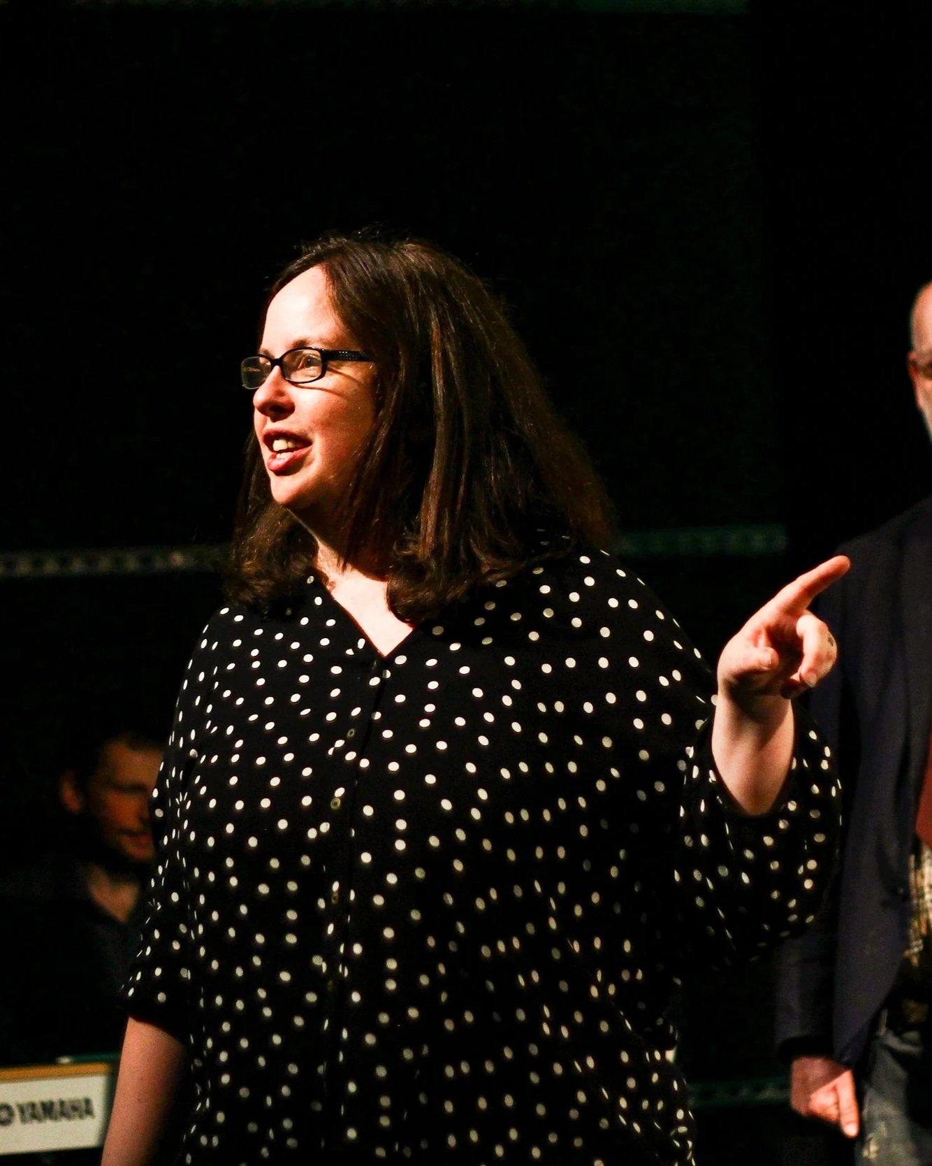 Headshot of Nicola Wydenback facilitating on stage wearing a black shirt with white polka dots