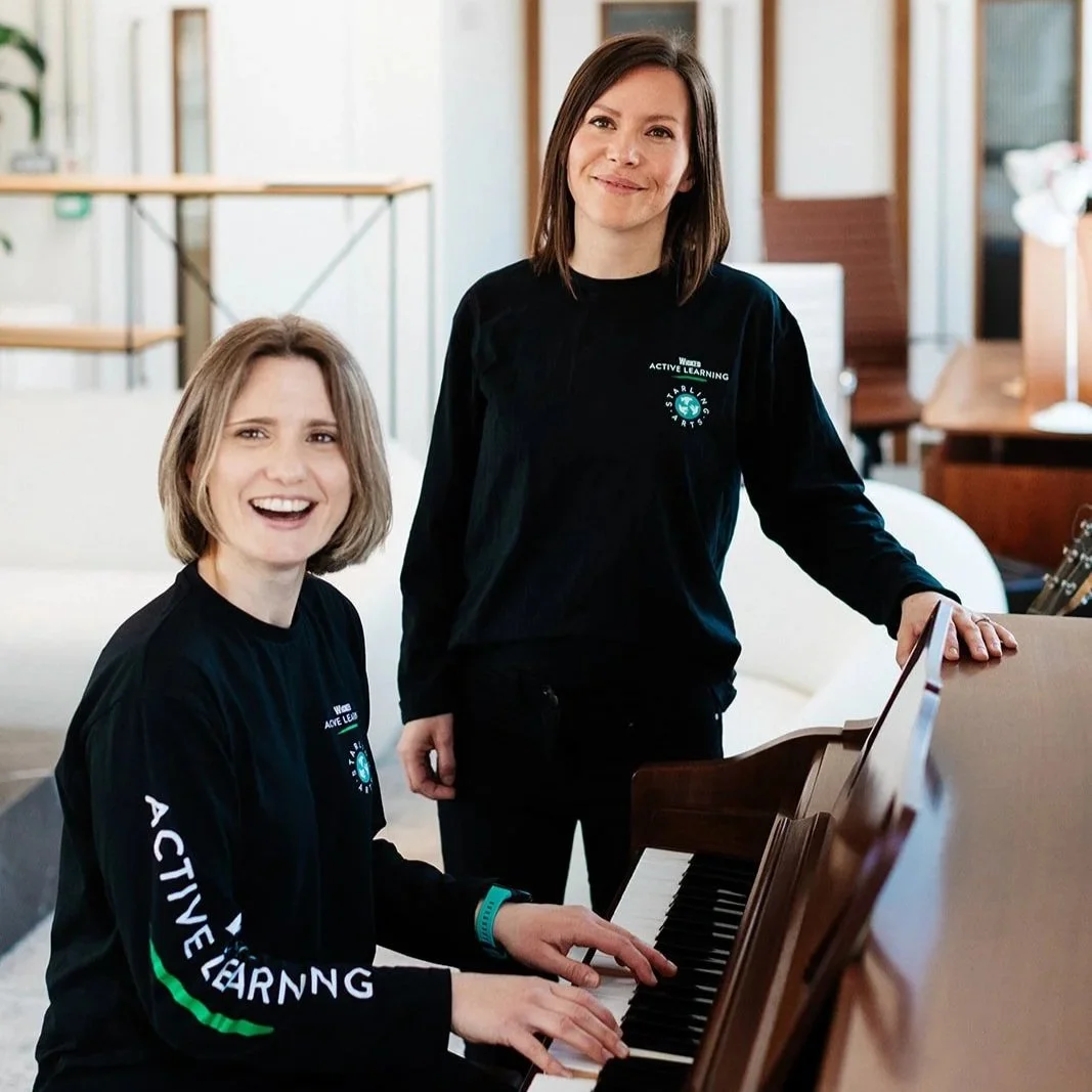 Anna Shields sits at the piano with Emily Garsin standing next to her