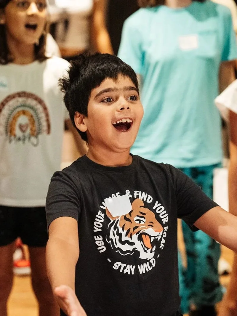 A young boy participating in an Official Wicked Workshop smiles, throwing his hand out in song