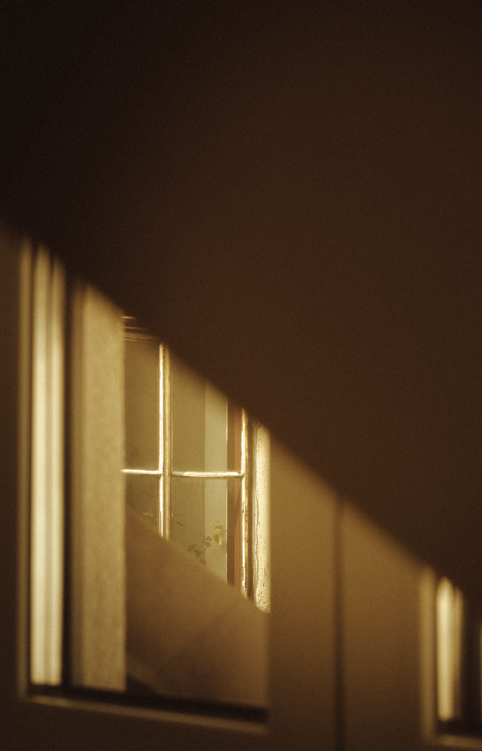 Looking through a small window set into a wall, with sunlight illuminating the window frame and a hint of greenery outside.