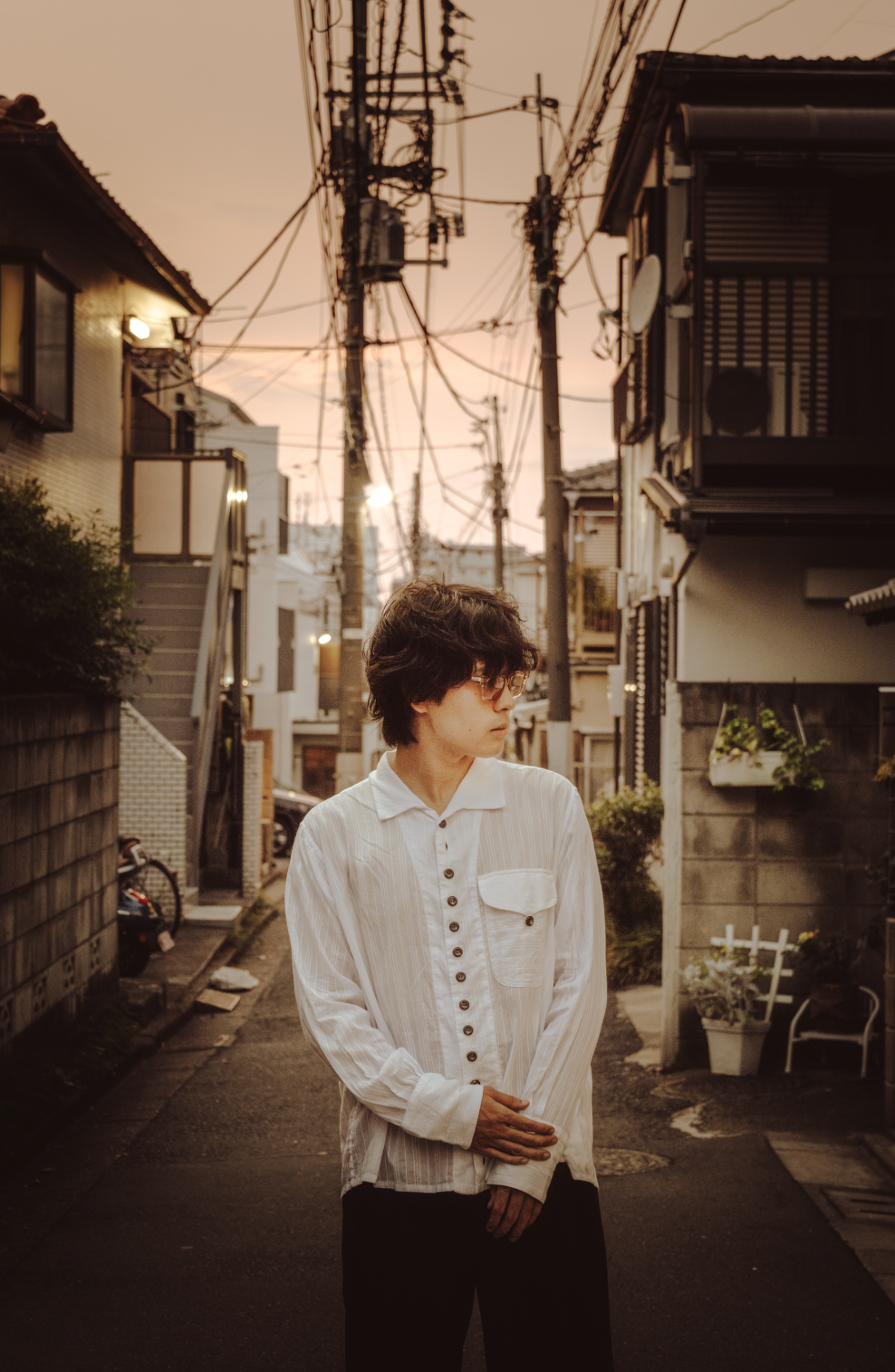 A person standing in a quiet alleyway during sunset with overhead power lines and residential buildings on either side.