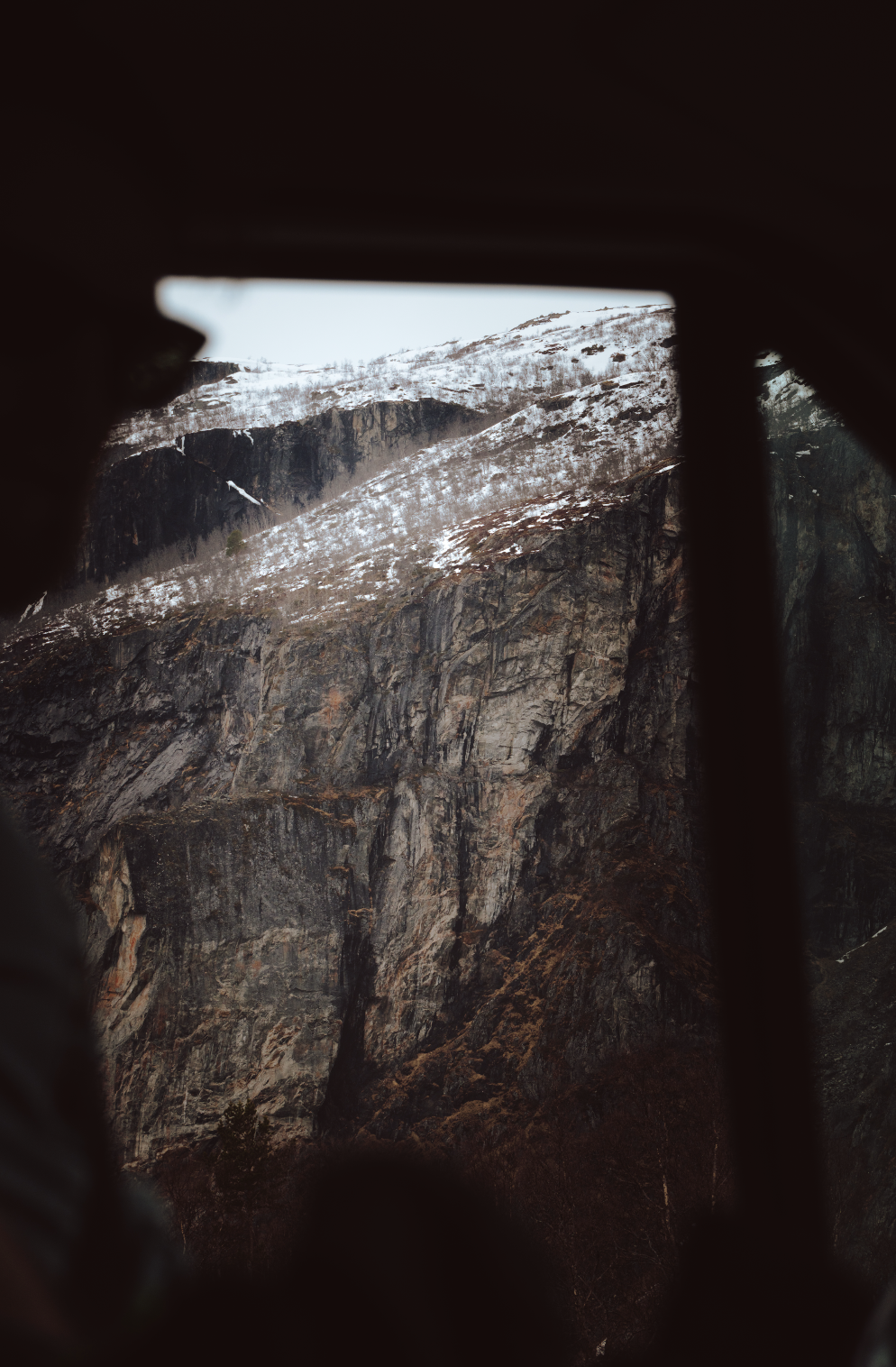 Mountain landscape seen through a window with dark framing and blurry edges, snow-capped peaks and rocky cliffs.