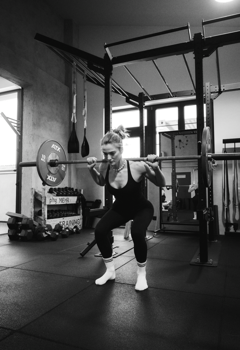 A woman lifting a barbell in a gym, black and white photo.