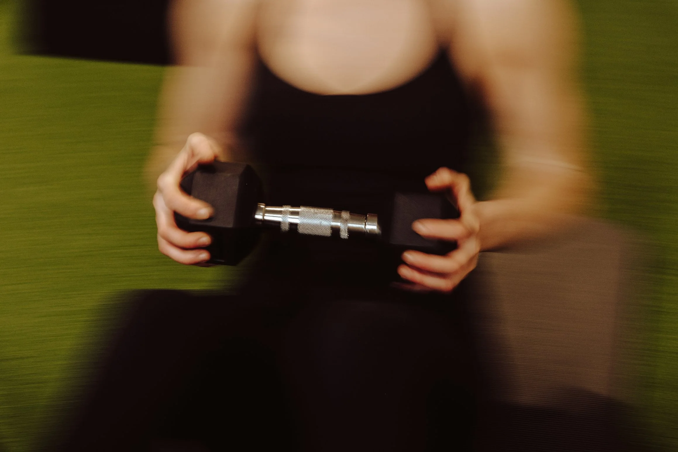 Person holding a black and silver dumbbell, wearing a black top, on a green surface.