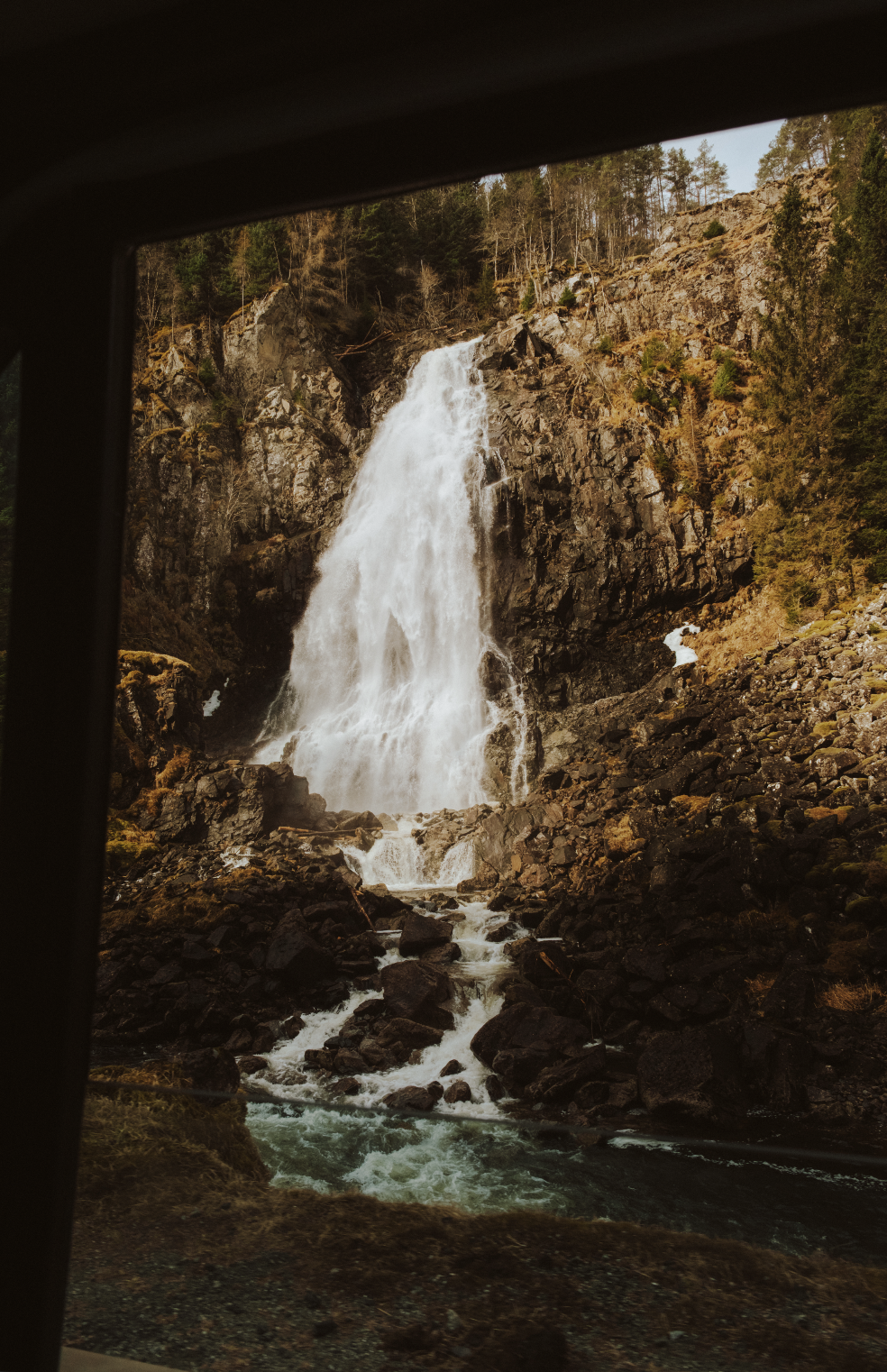 Waterfall cascading down a rocky cliff with trees in the background.