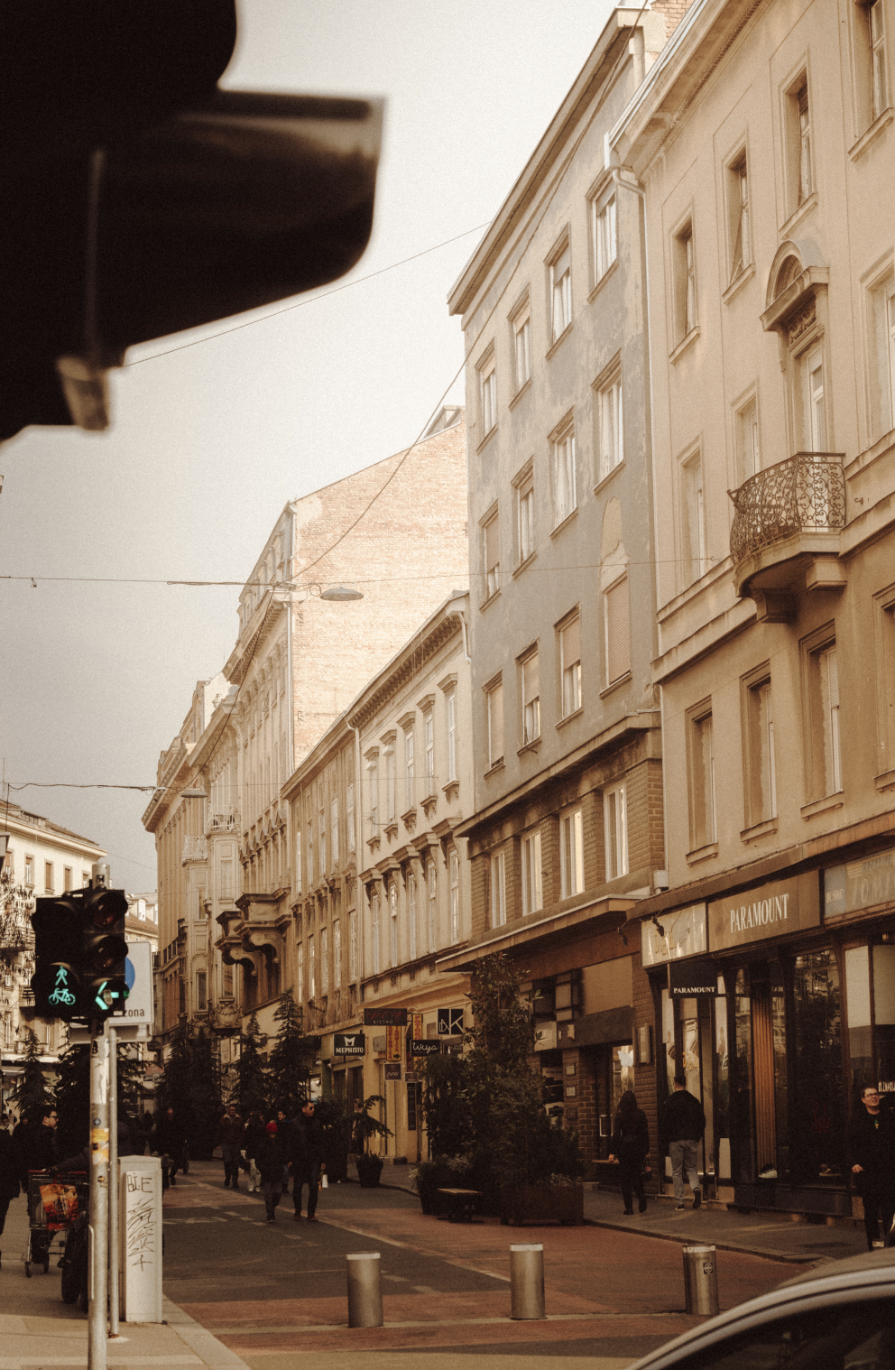 City street scene with pedestrians, storefronts including a Paramount store, and architecture with multiple stories.