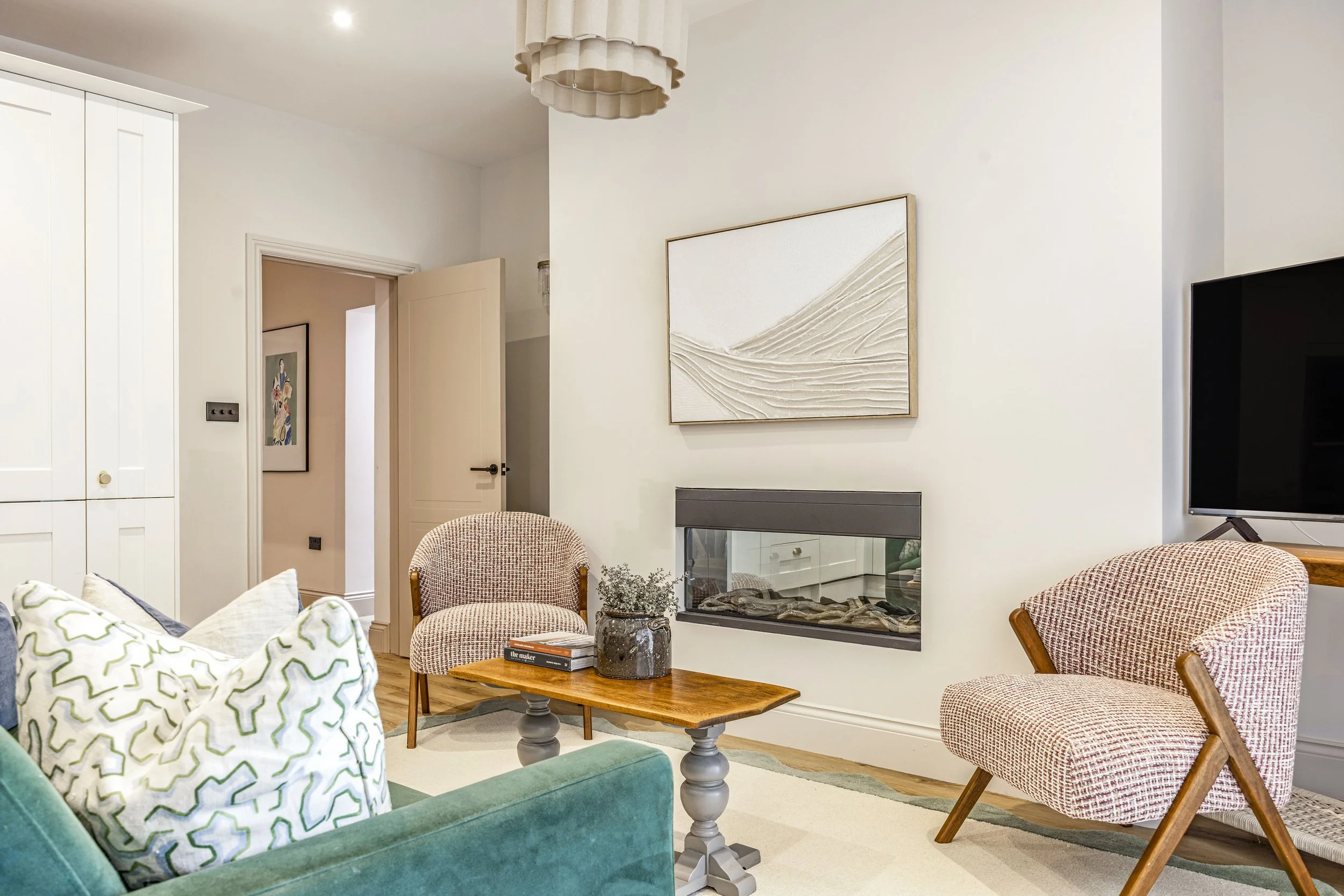Living room with white walls, wooden furniture, beige and patterned chairs, a green sofa, a coffee table, wall art, a fireplace, and a TV.