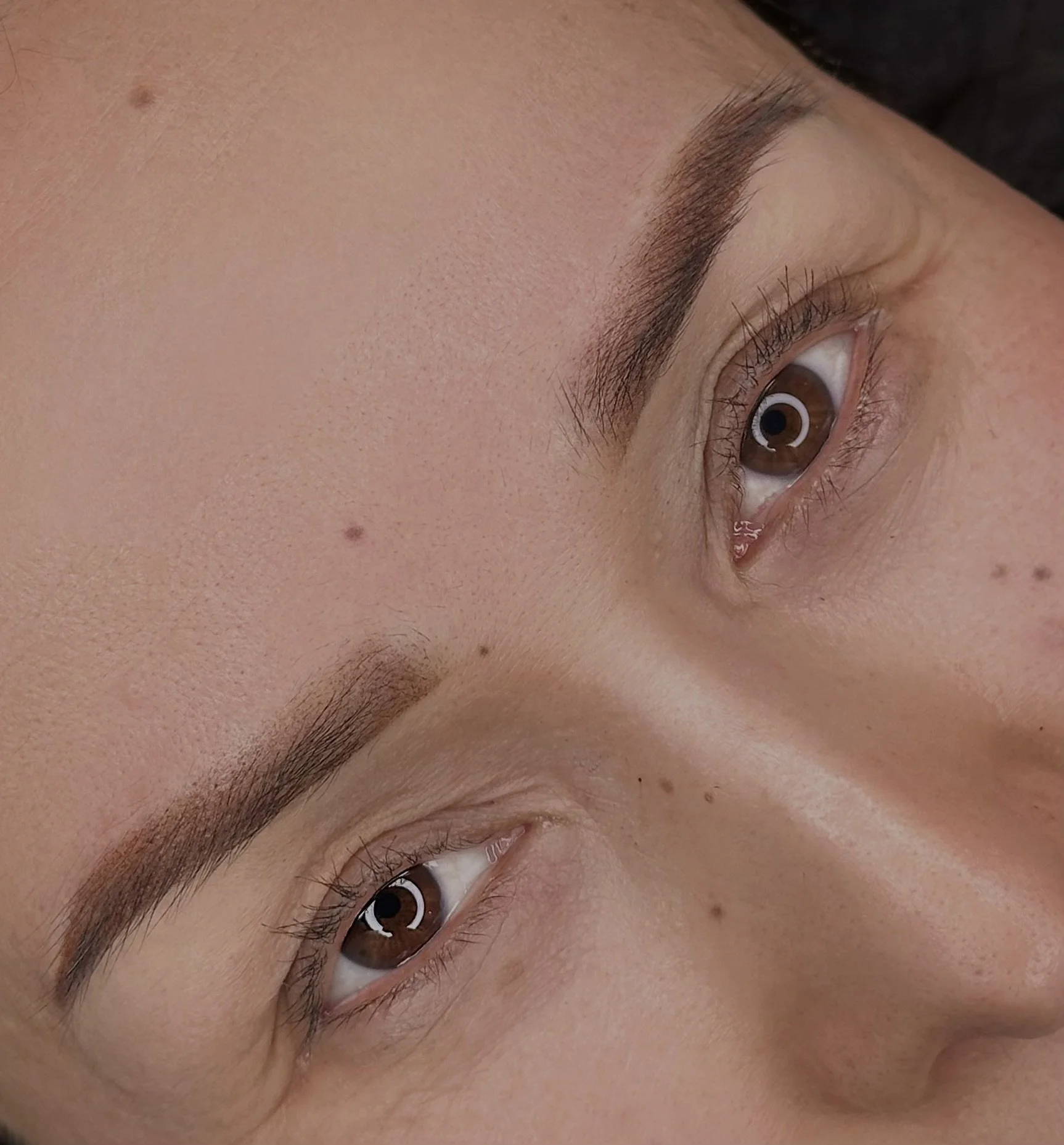 Close-up van een menselijk gezicht met bruin oog, rechte wenkbrauw, lichte huid, drie moedervlekken en lichte sproetjes.
