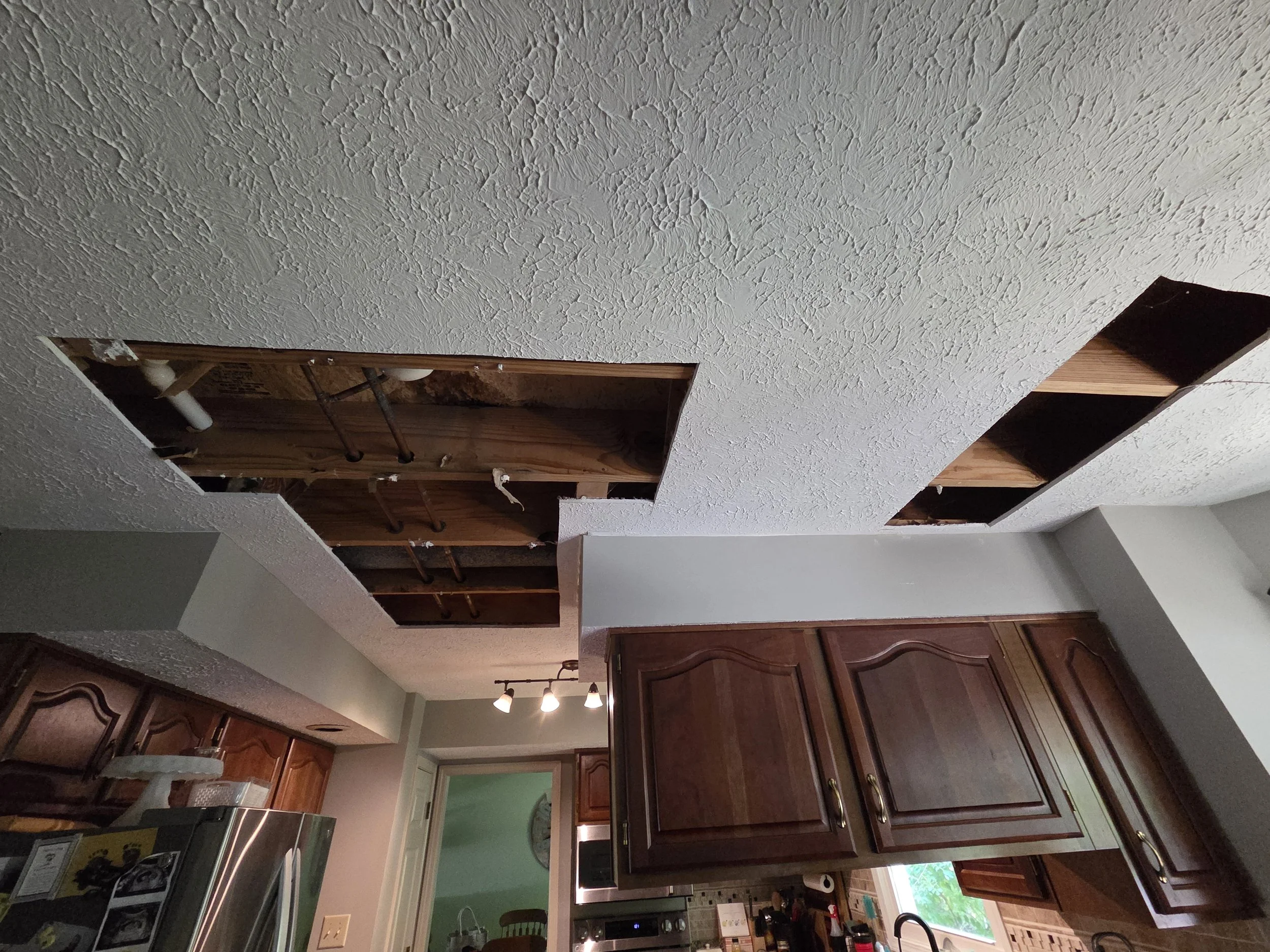 Kitchen with unfinished ceiling, open ceiling panels showing wooden framing and pipes, dark wood cabinets, electric stove, and green wall.