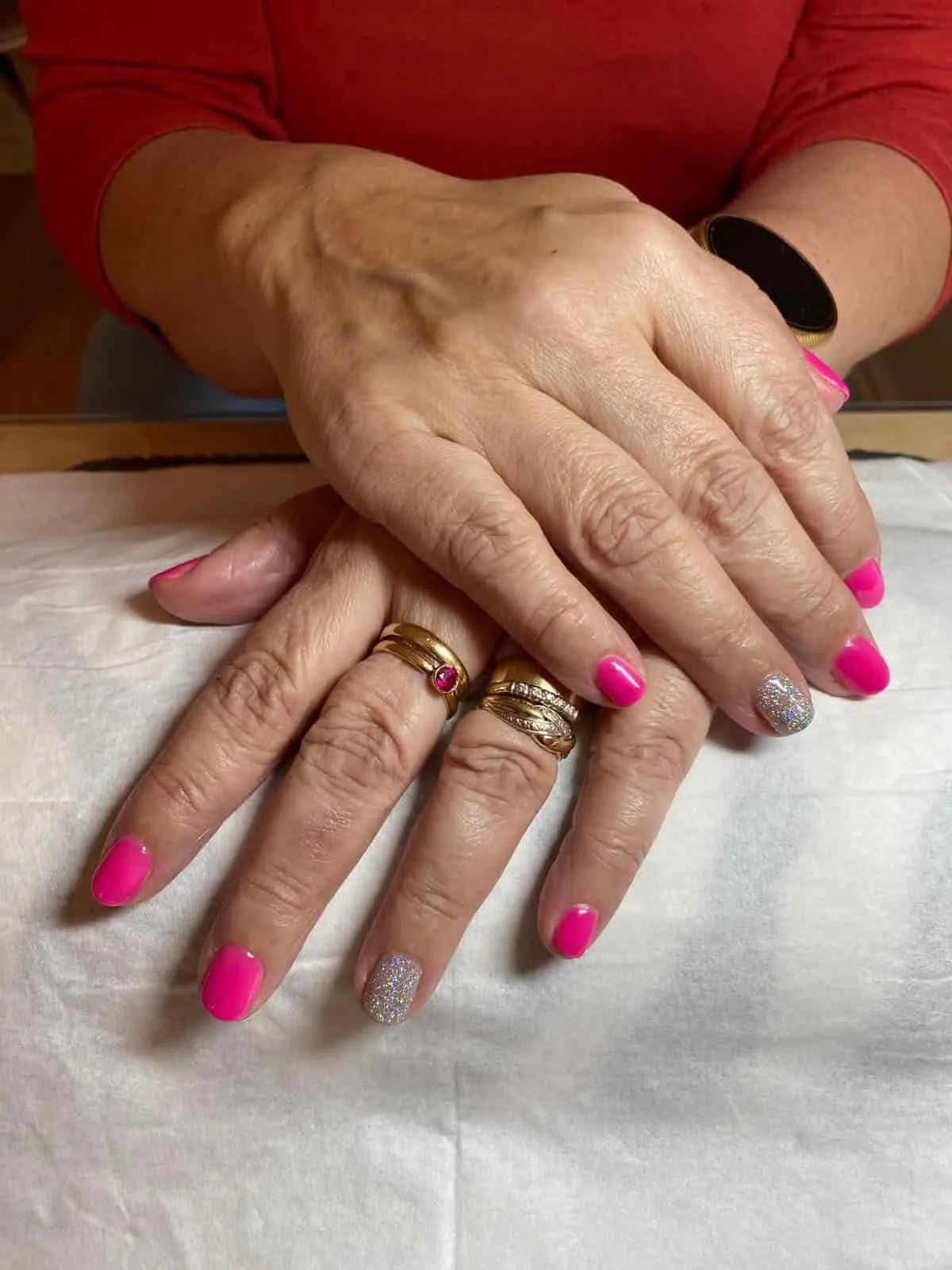 Kaksi kättä, joissa on useita sormuksia, ja kynnet on maalattu pinkiksi ja hopean glitteriä sisältäväksi.
