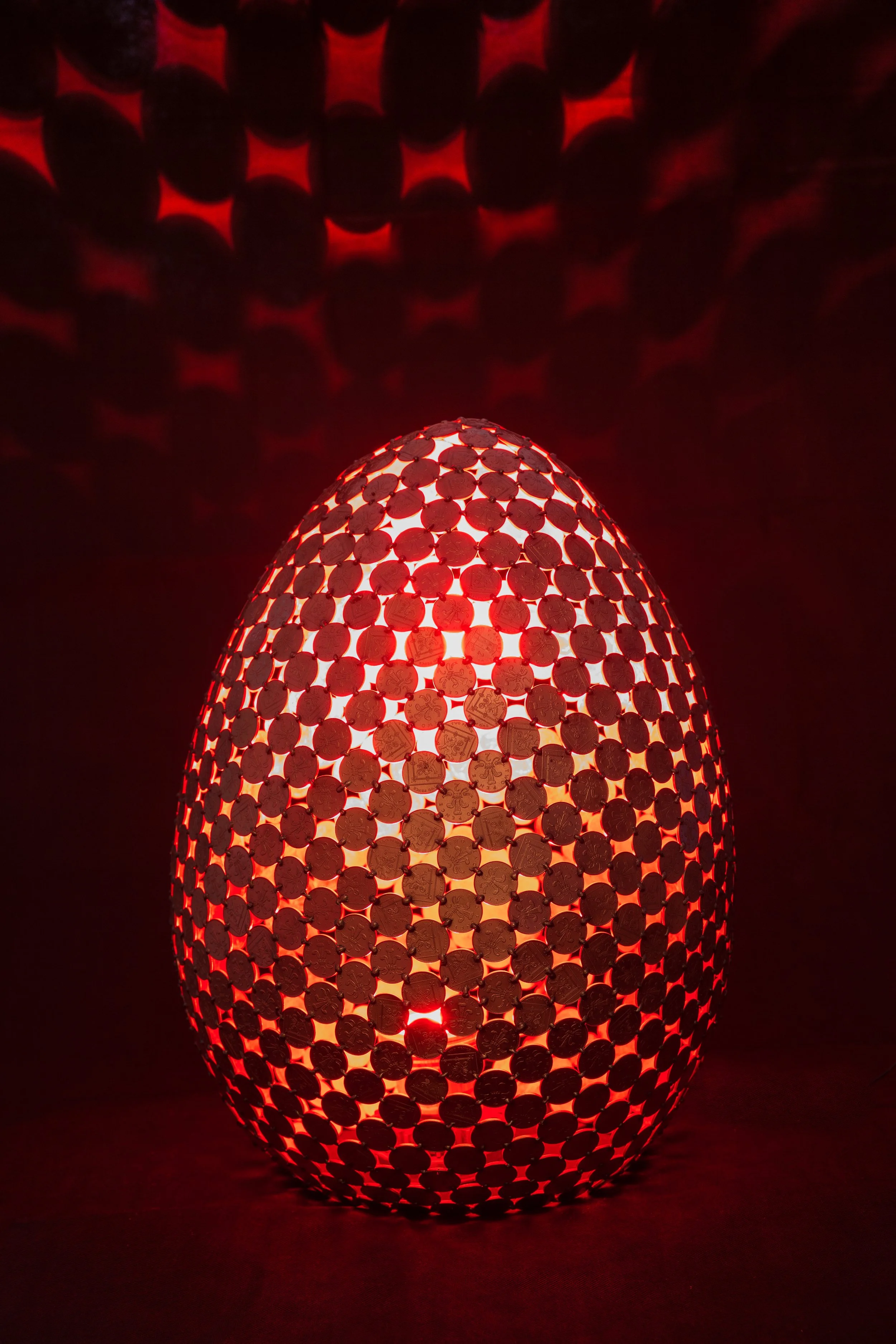 Egg Lamps are large egg-shaped sculptures made from welded 2p coins that emit light with a color-changing controller. Handmade by Shaun Gagg, each piece may vary, and customizations are available.
