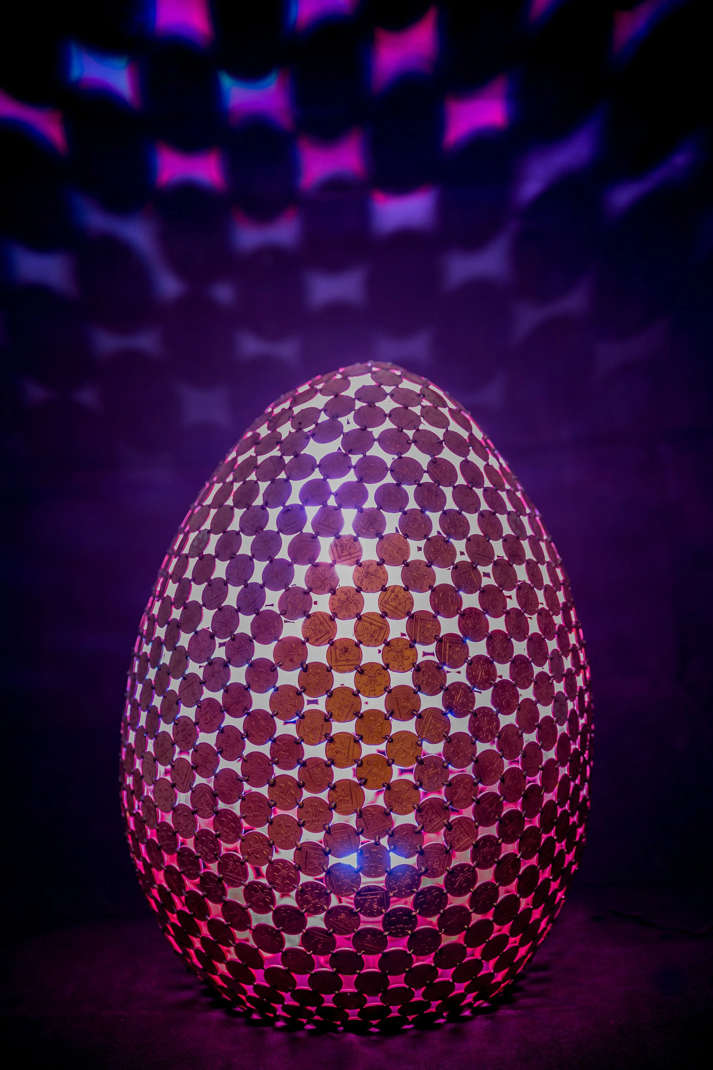 Egg Lamps are large egg-shaped sculptures made from welded 2p coins that emit light with a color-changing controller. Handmade by Shaun Gagg, each piece may vary, and customizations are available.