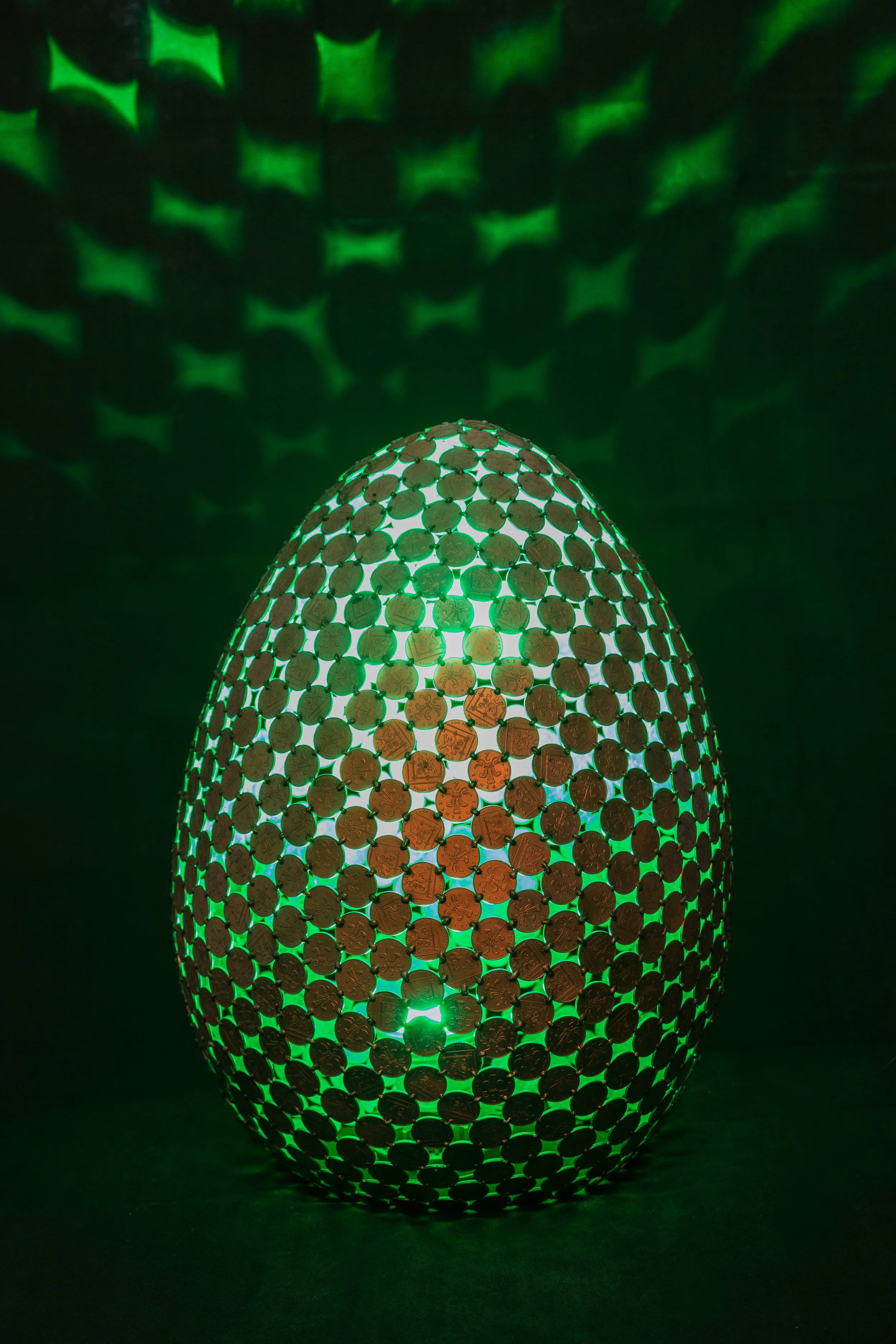 Egg Lamps are large egg-shaped sculptures made from welded 2p coins that emit light with a color-changing controller. Handmade by Shaun Gagg, each piece may vary, and customizations are available.