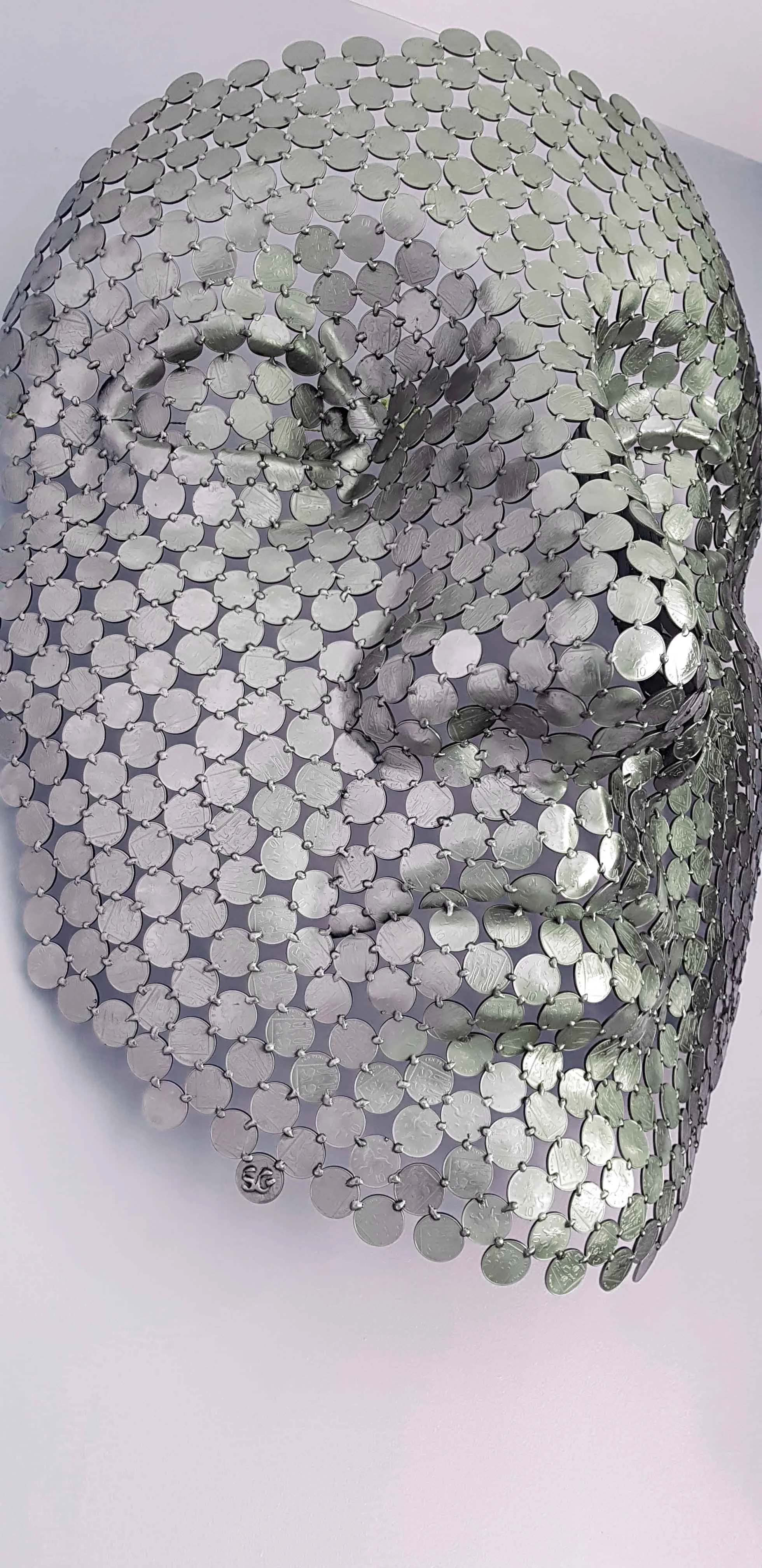 A magnificent face sculpture by Shaun Gagg crafted from 10p coins. This intricate piece captures striking facial features and texture, designed to hang elegantly on the wall,