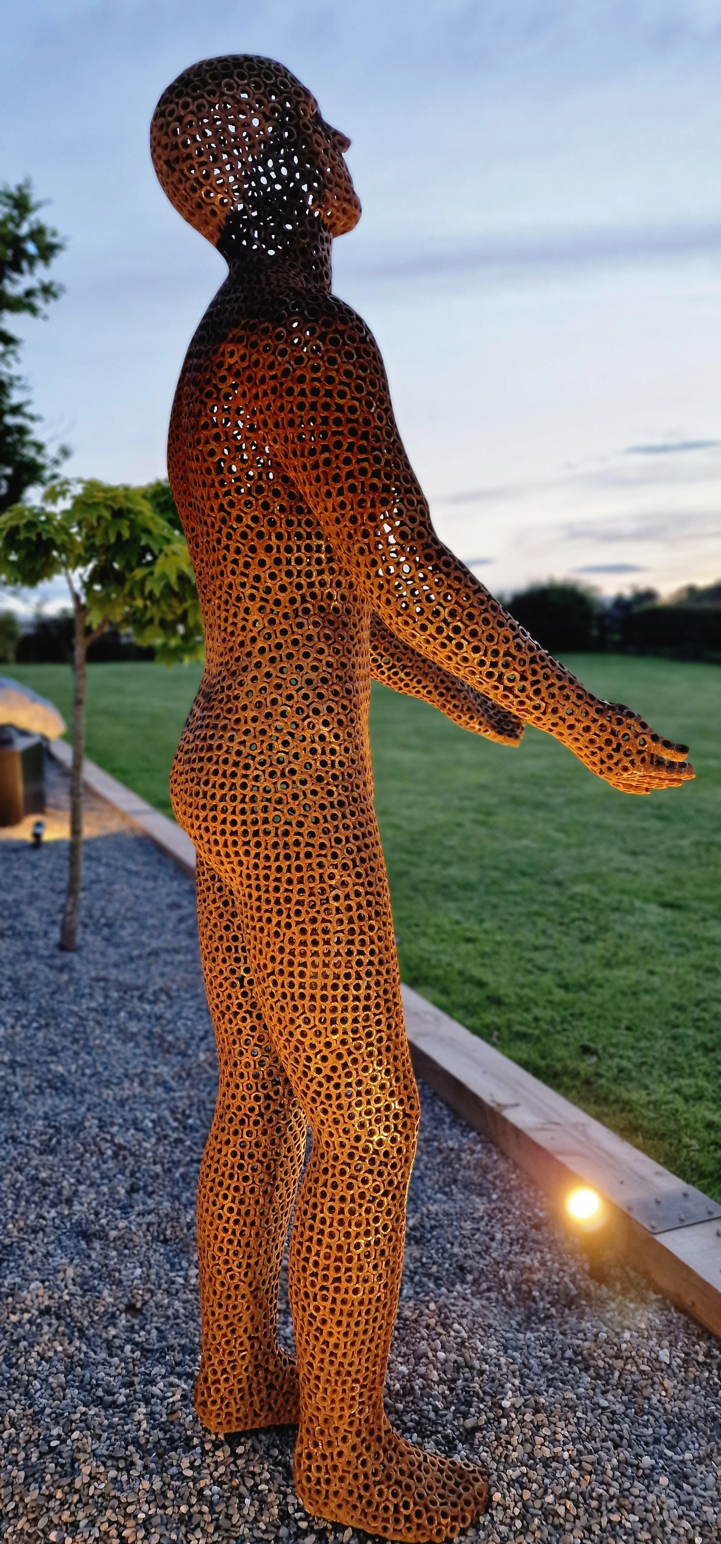 This is a life-size metal sculpture made from nuts depicting a man looking up into the sky with his hands held out in front of him trying to fill the rain